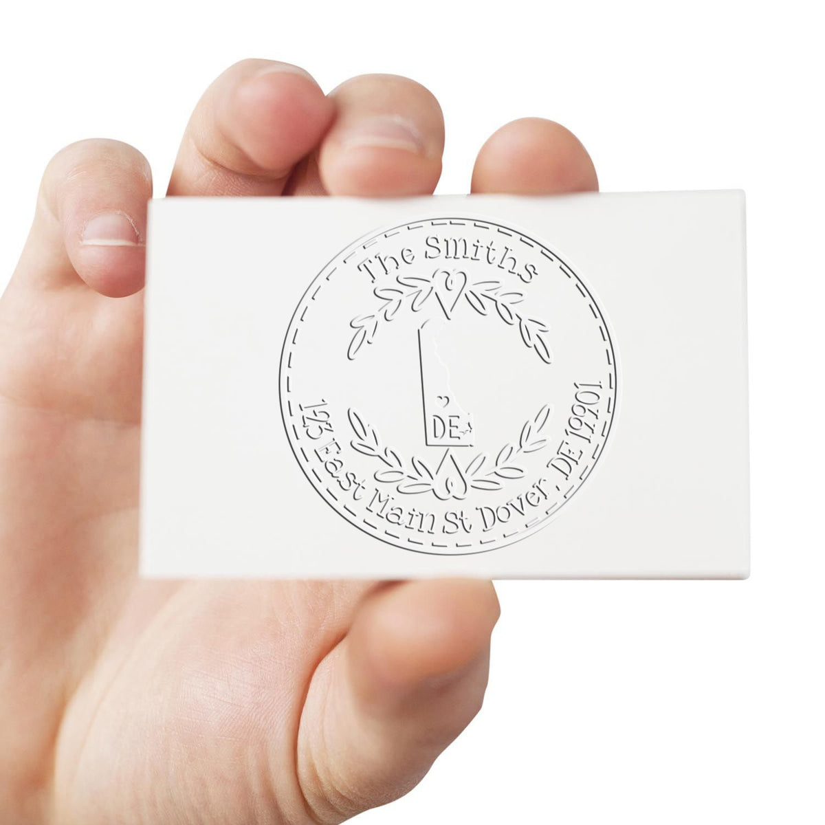 Hand holding white custom stamp seal with round engraved Smiths family crest and address in gray
