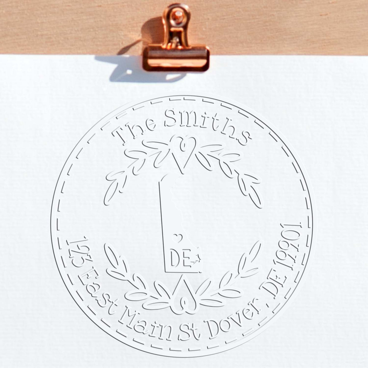 Copper binder clip holds white paper with embossed circular stamp seal reading The Smiths, with laurel wreath and house logo.