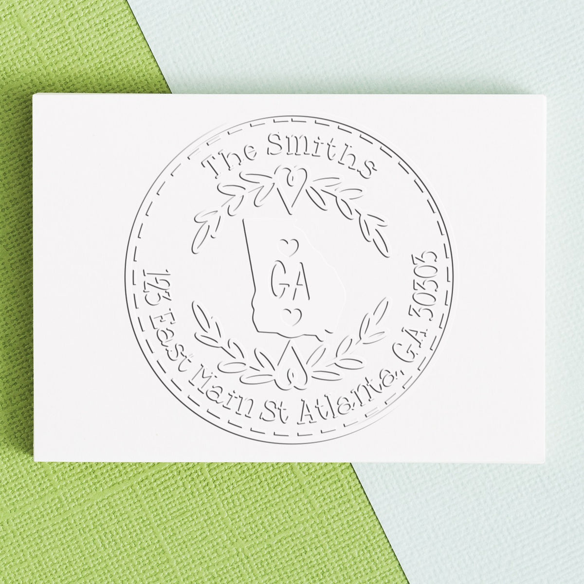 White embossed custom stamp and seal with circular Georgia wreath design on green and white textured background.
