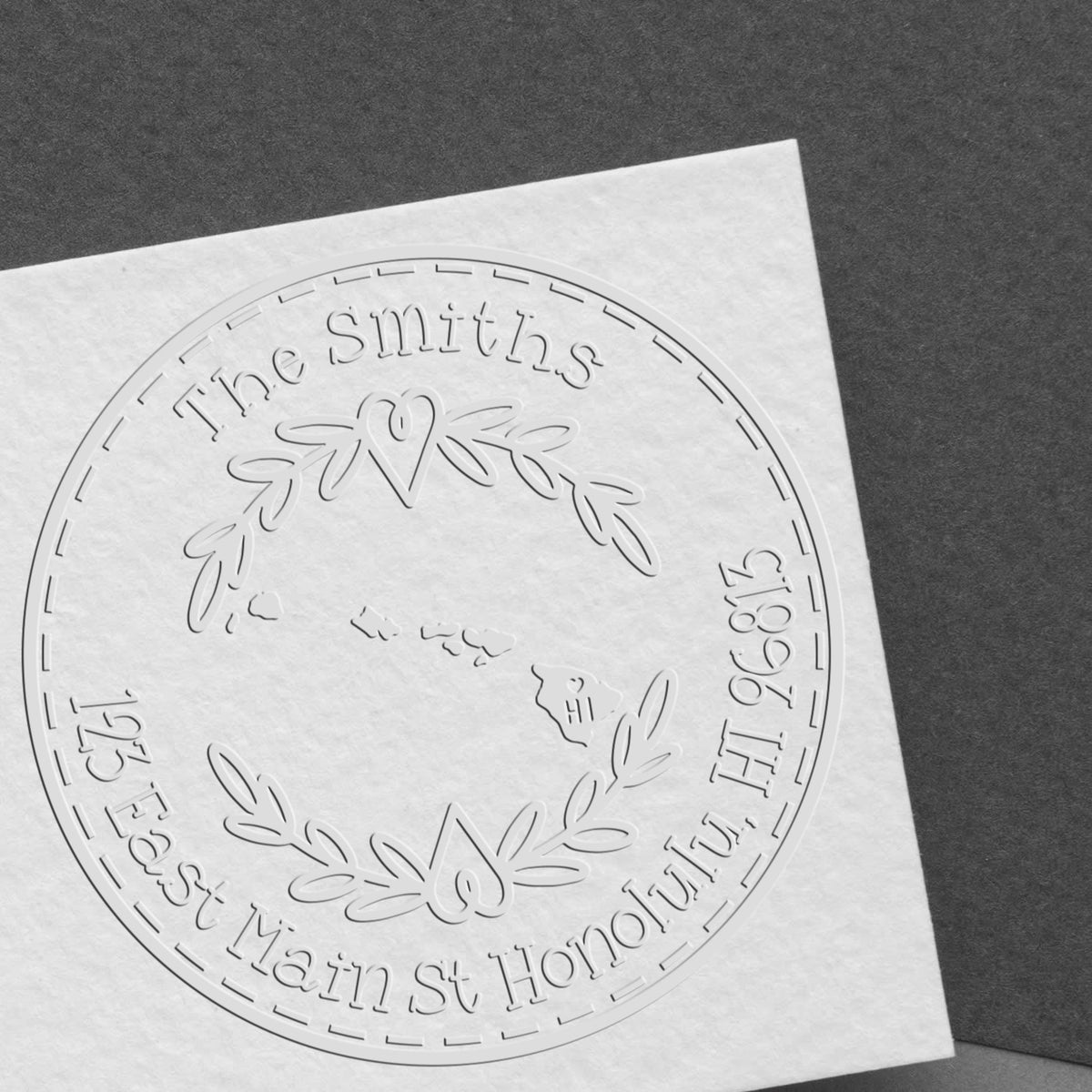 Embossed white custom stamp seal with laurel wreath and heart, reading The Smiths and 123 East Main St Honolulu HI.