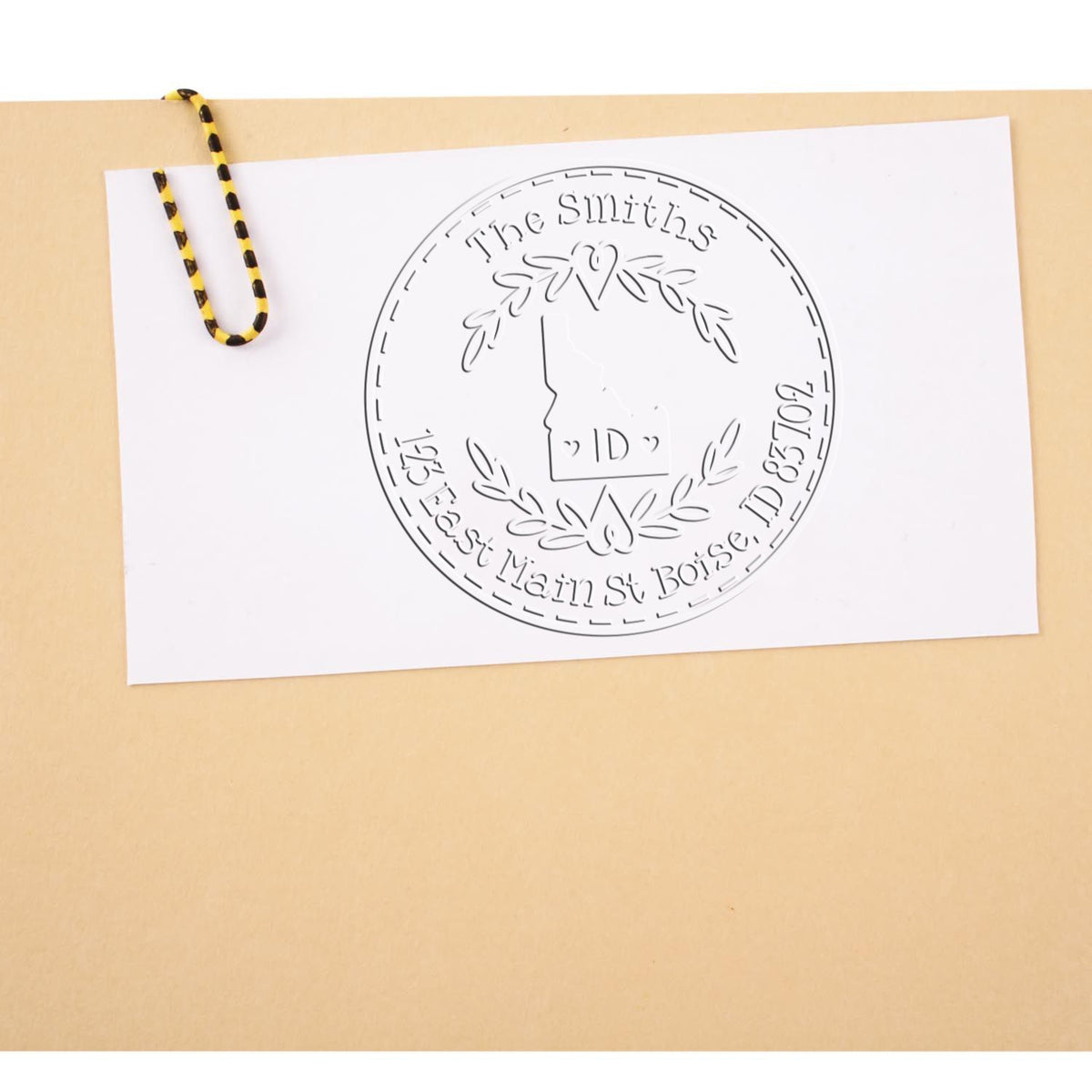 Custom round white seal stamp with embossed logo, clipped by a black-and-yellow binder clip on beige background.