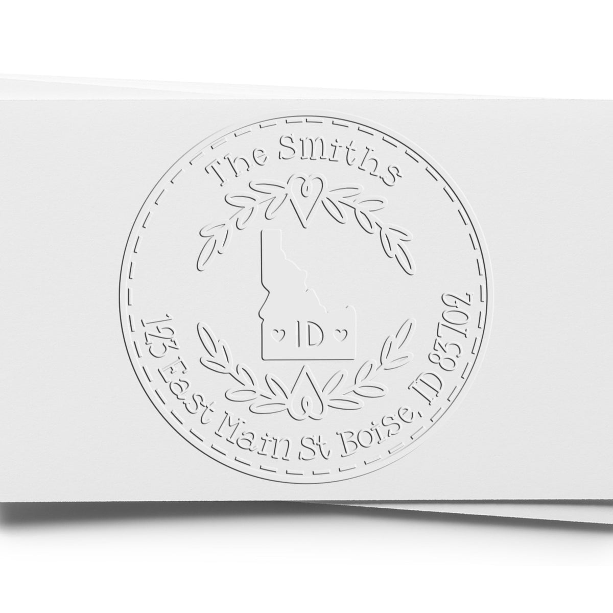 White embossed custom seal stamp with The Smiths, Idaho outline, laurel wreath, and ID initials on white paper.