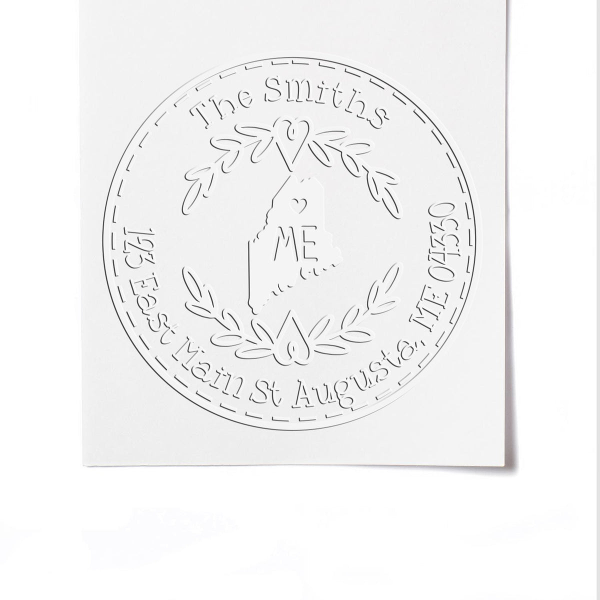 White embossed circular stamp seal with laurel wreath, heart, and Maine outline on white paper.