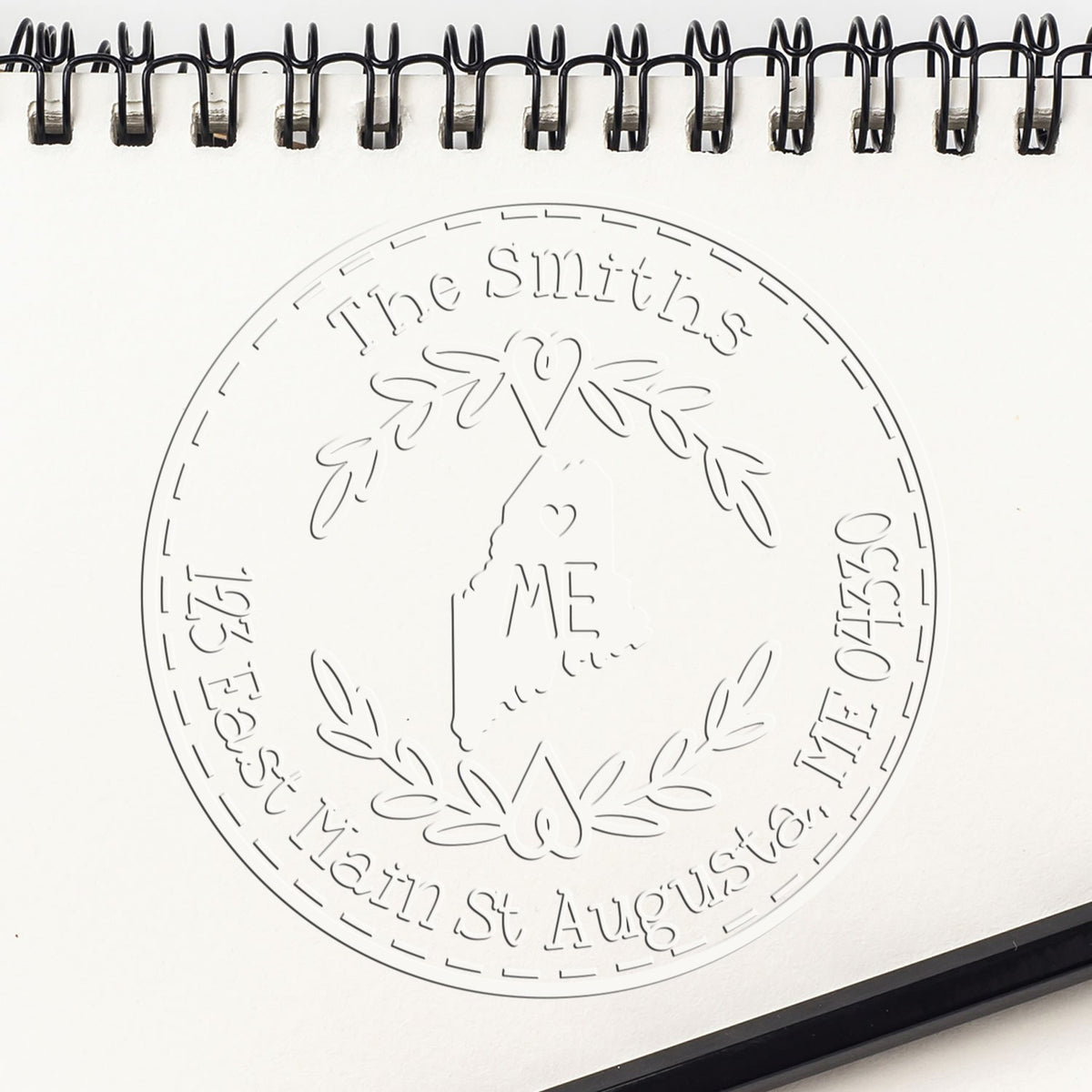 Embossed stamp and seal design for The Smiths on white notebook page, with black spiral binding and laurel wreath details.