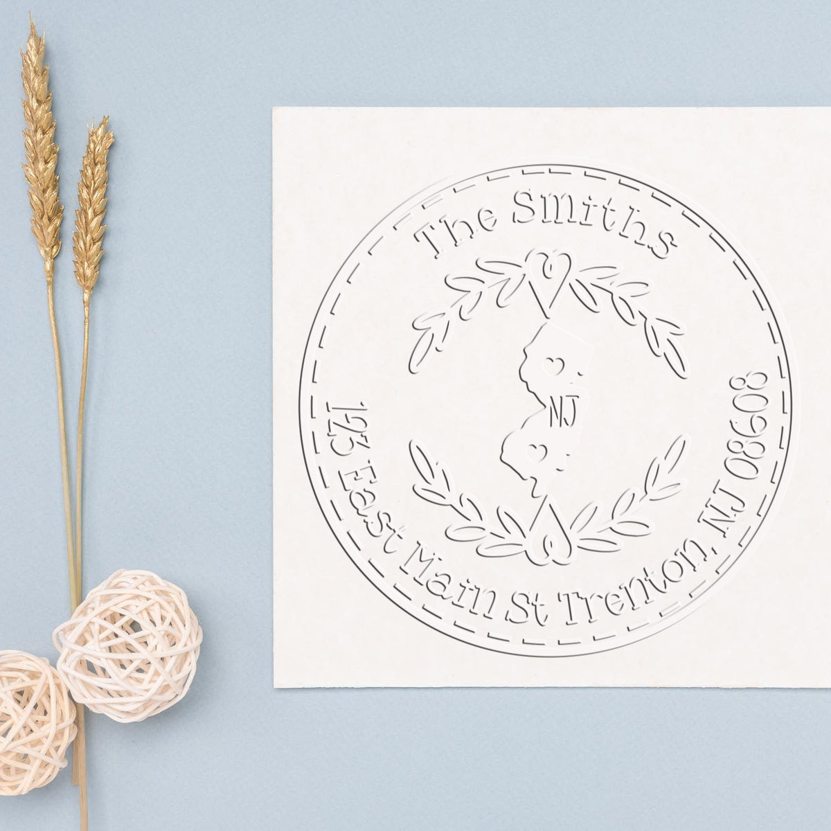 White custom stamp seal with circular The Smiths design on pale blue, beside gold wheat stems and white wicker balls.