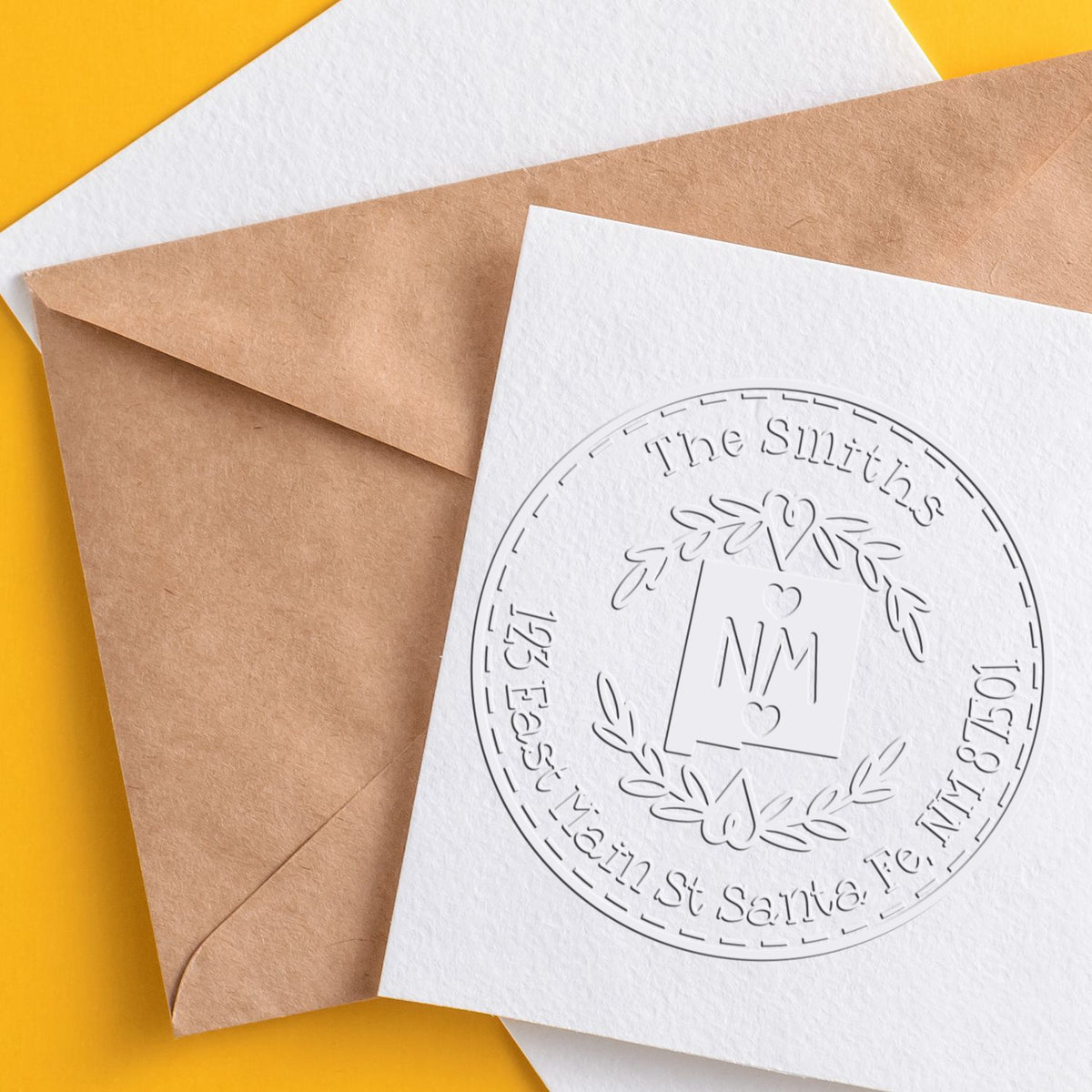 Custom embossed stamp and seal on white card over kraft envelopes, with circular monogram and yellow background.