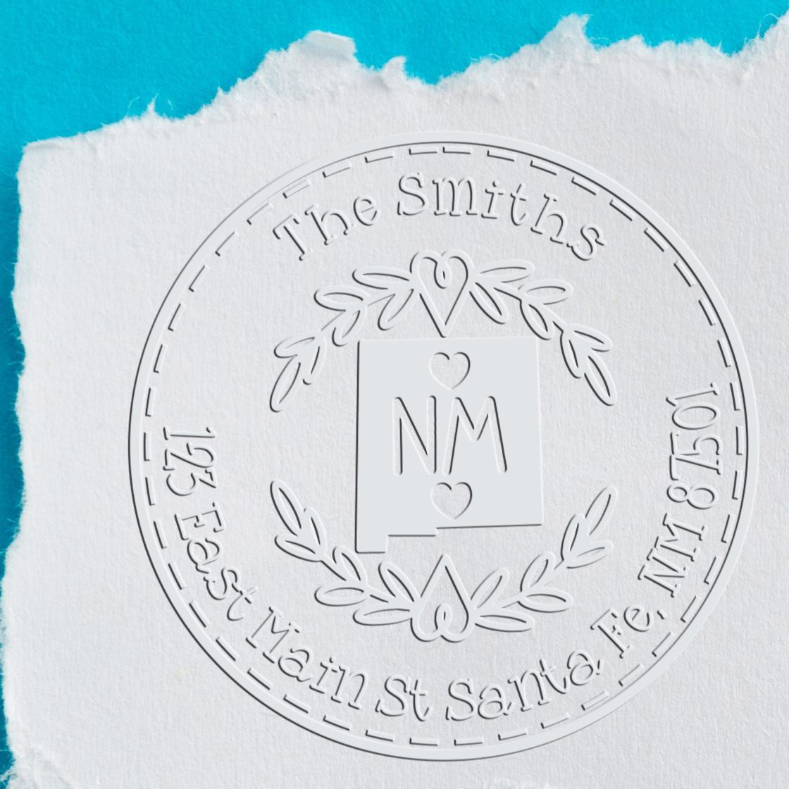 Embossed white round custom stamp seal with laurel wreath, NM monogram and The Smiths on white paper over teal background.