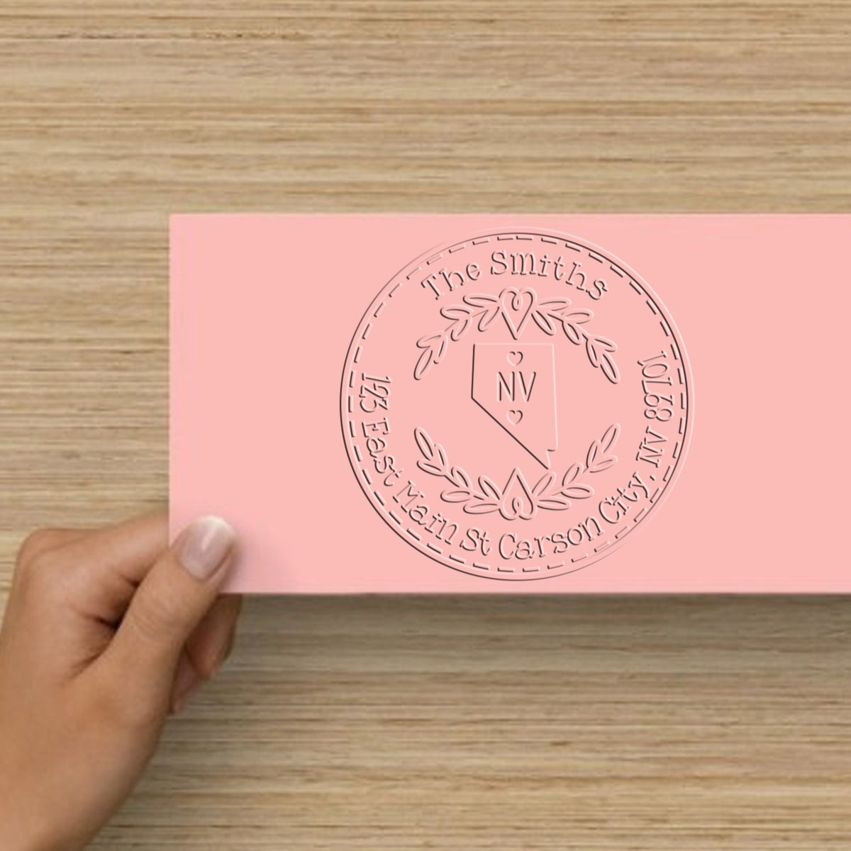 Hand holding a pink custom stamp and seal card with circular embossed family monogram and Nevada outline.