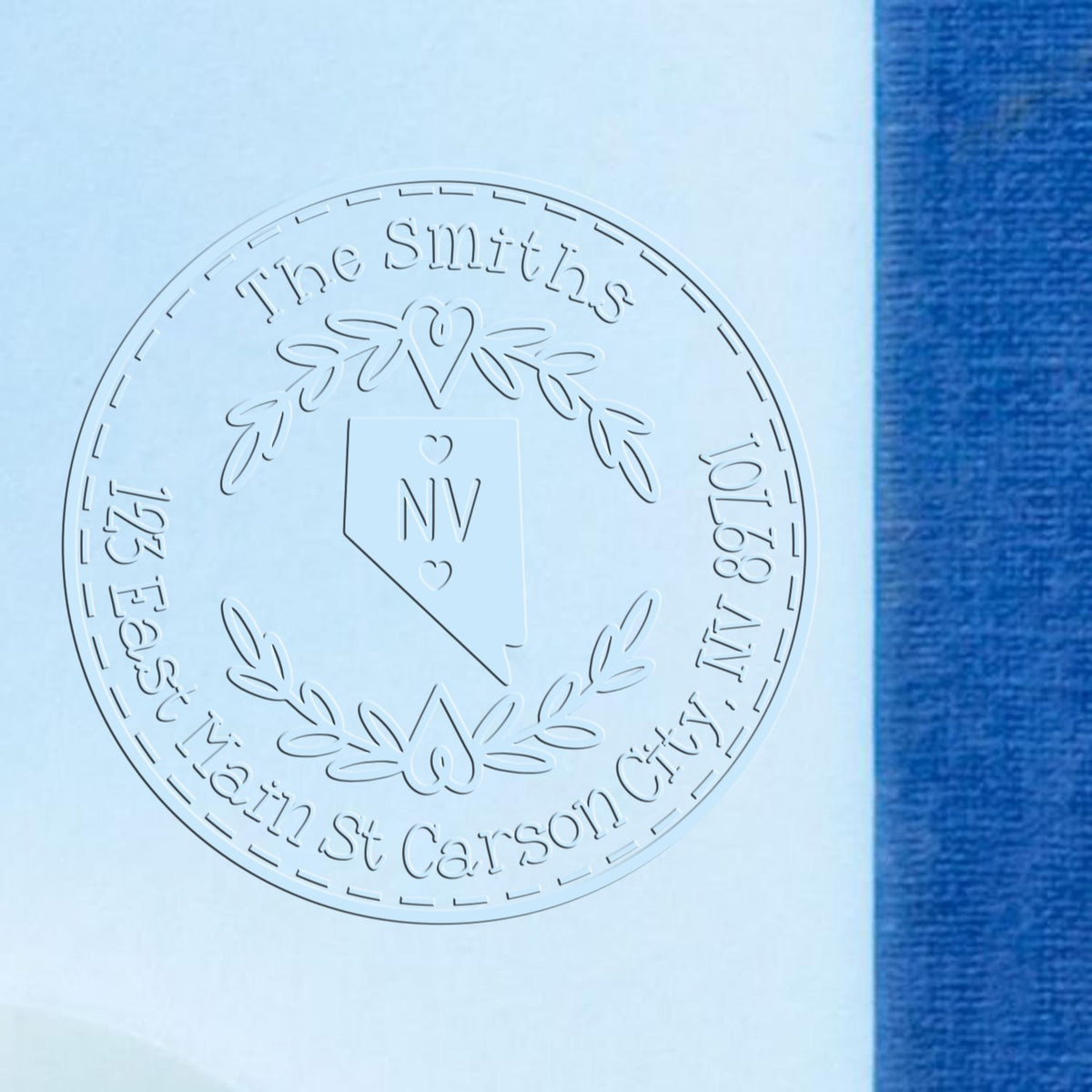 Embossed circular stamp seal for The Smiths, with Nevada outline and laurel wreath on light blue paper beside blue fabric.