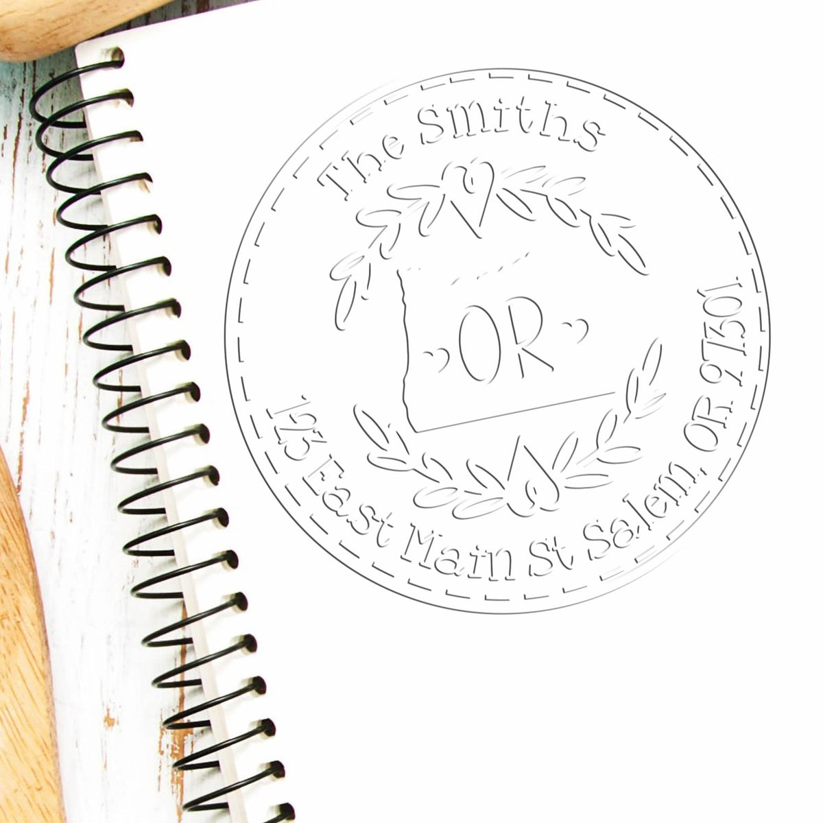 Custom circular stamp seal for The Smiths with floral wreath, OR center, on a white spiral notebook.