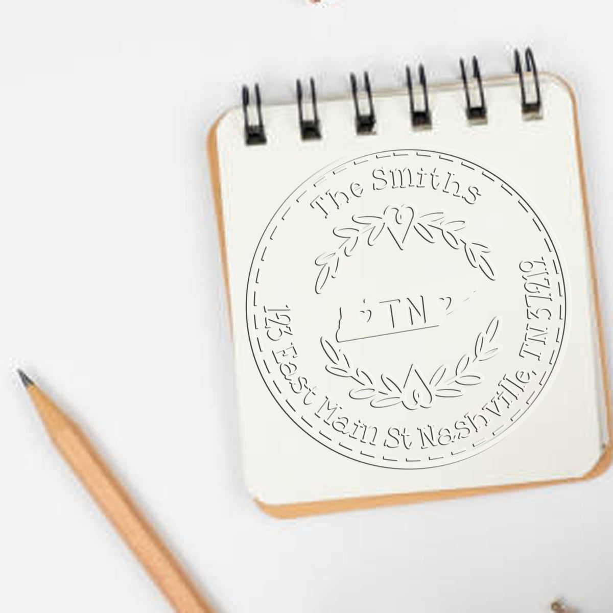 Cream spiral notebook with custom embossed family seal stamp reading The Smiths, TN, and Nashville, beside a wooden pencil.
