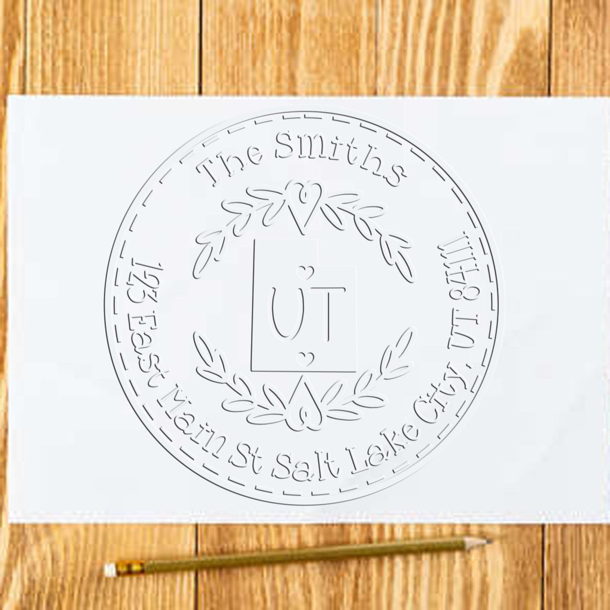 White circular custom stamp seal with laurel wreath, UT monogram, and embossed name text on a wood background.