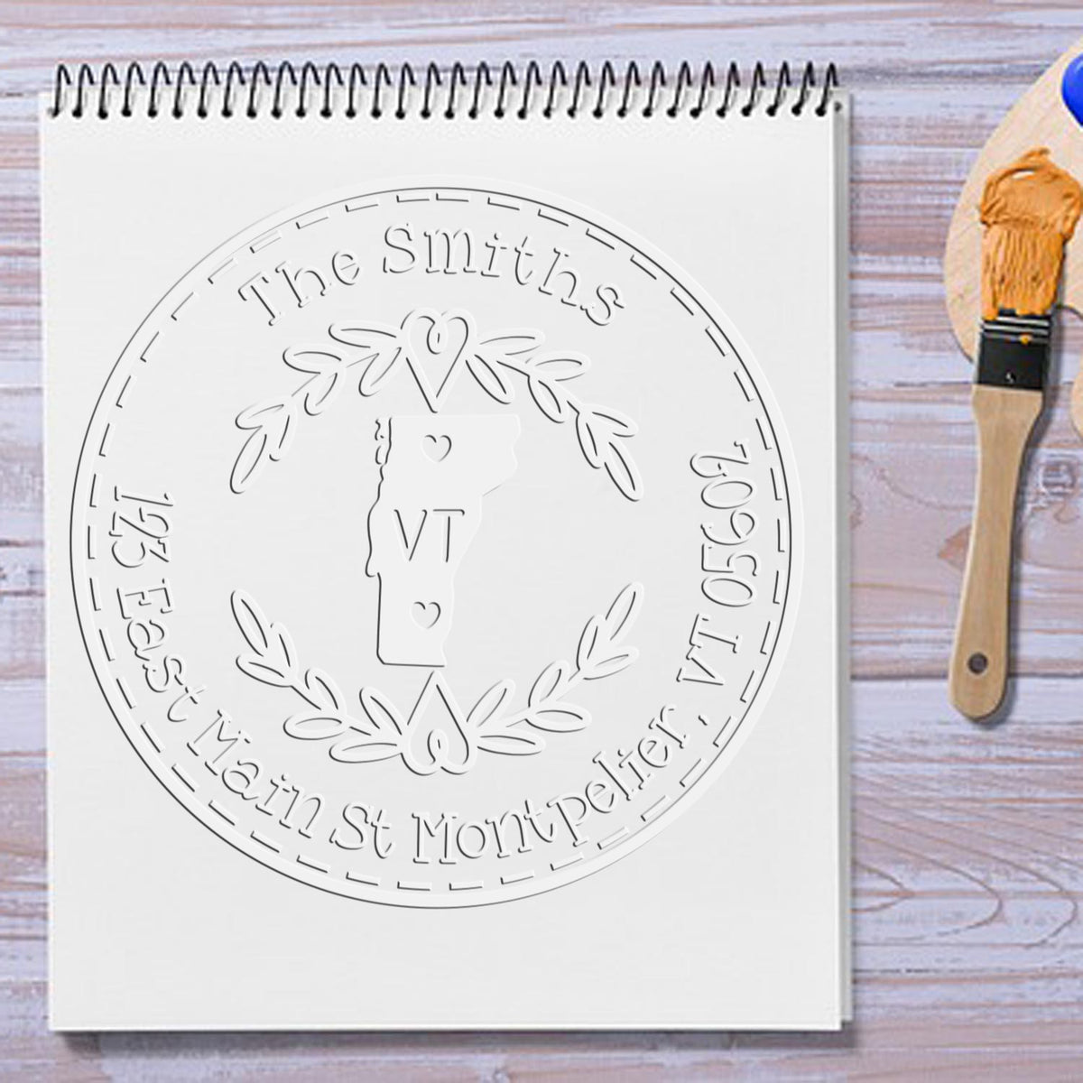 Custom white embossed stamp seal on spiral notebook, featuring Vermont outline, laurel wreath, and The Smiths text.