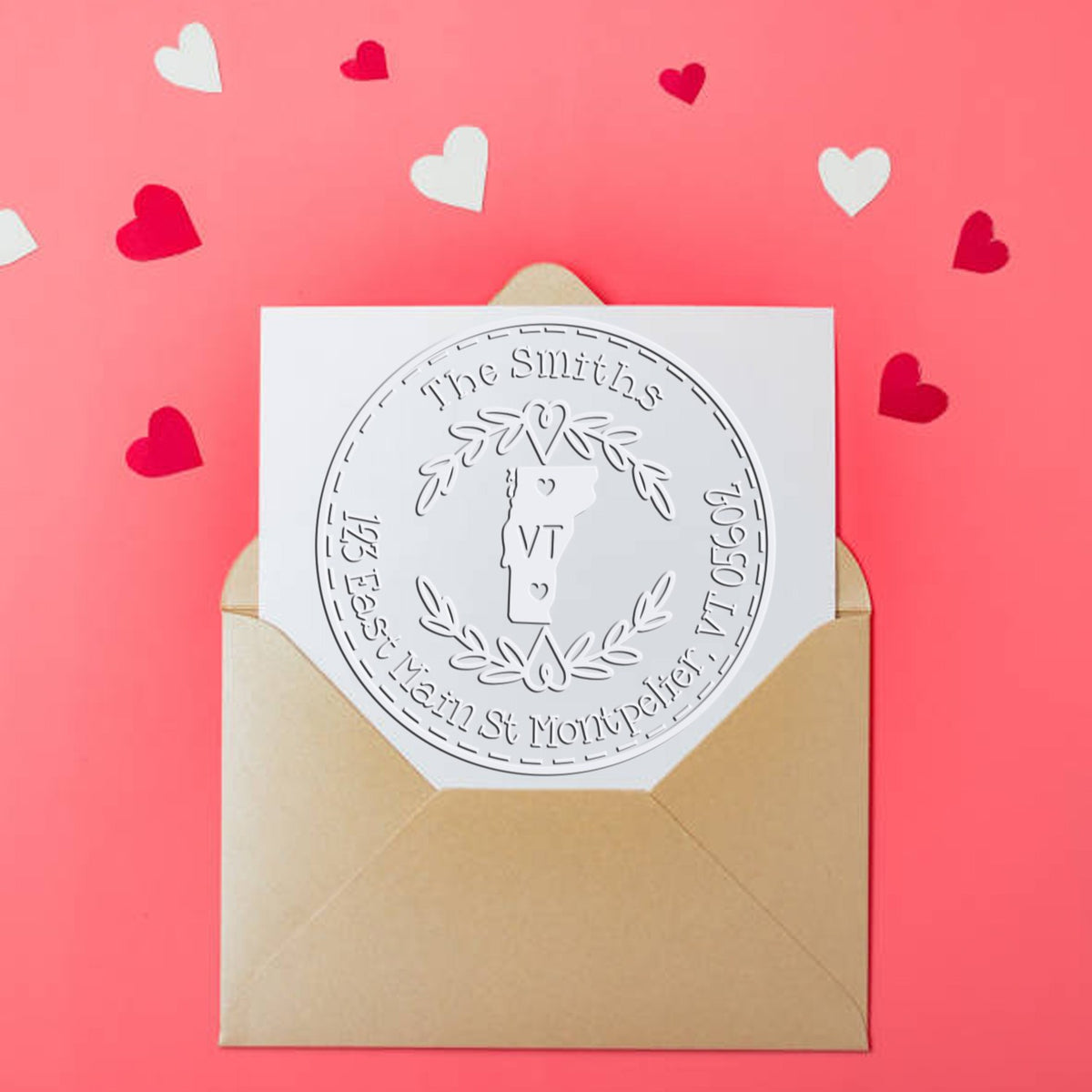 Beige envelope with custom embossed silver heart seal on white card, set on a pink background with red and white hearts.
