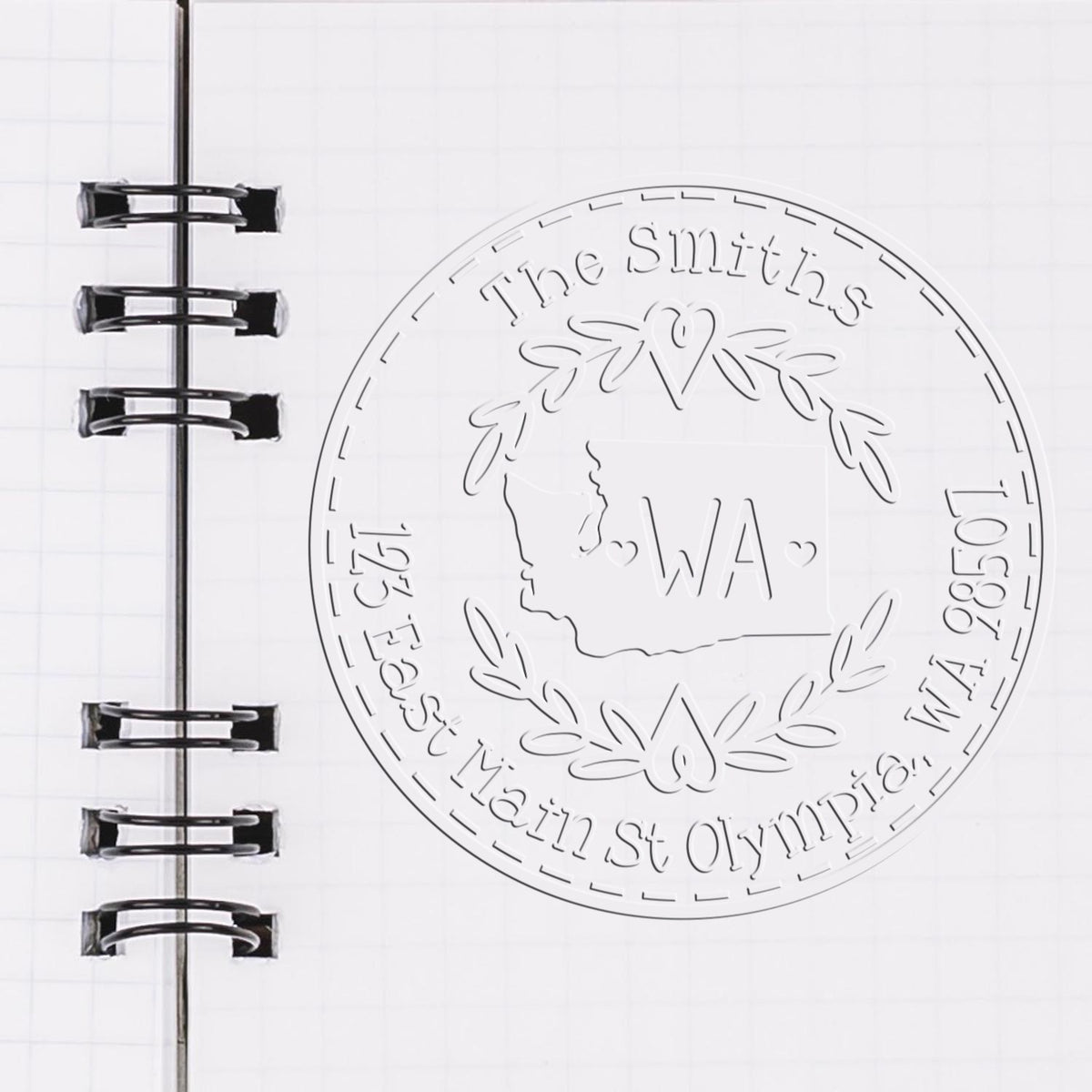 Clear embossing stamp seal with circular The Smiths Washington state design on white notebook page with black spiral binding.