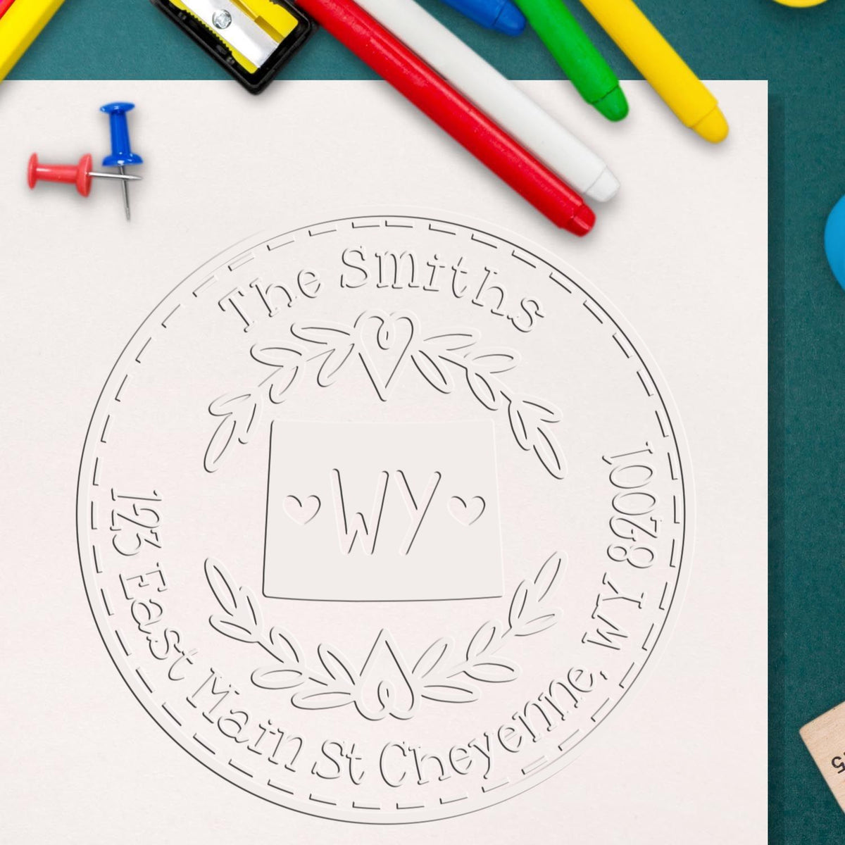 White custom stamp and seal design for The Smiths with WY, hearts and laurel, surrounded by colorful markers and push pins.
