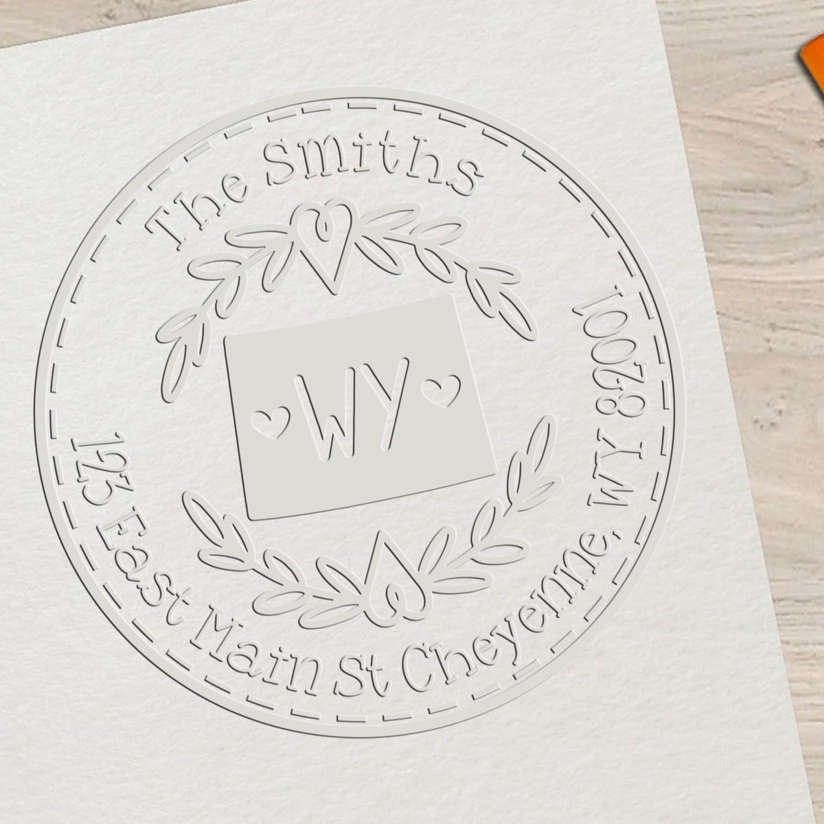 White embossed custom stamp seal on white paper, featuring a laurel wreath, hearts, and The Smiths with WY monogram.