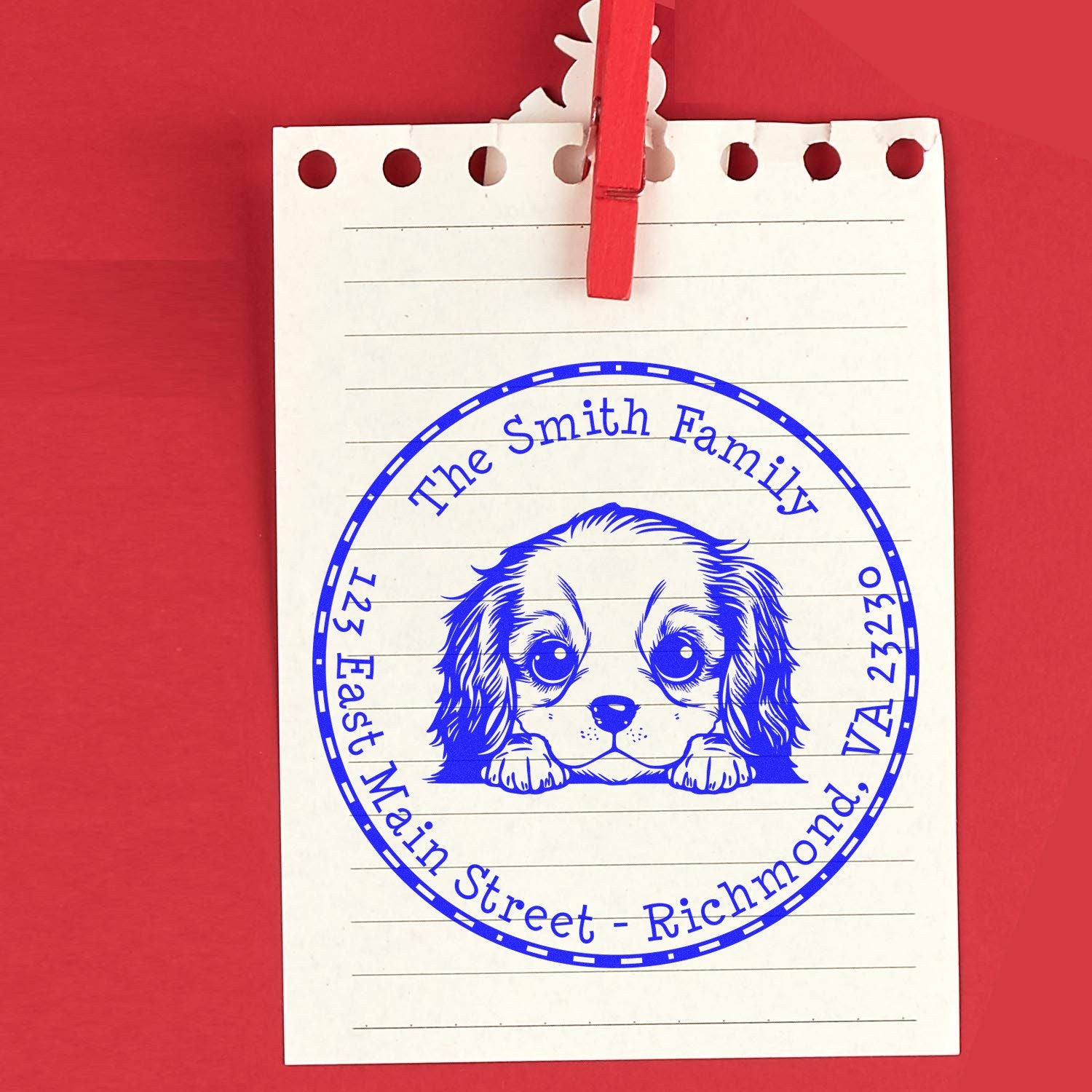 Blue circular rubber stamp seal with a dog illustration on lined white paper, clipped with a red clothespin on a red background.