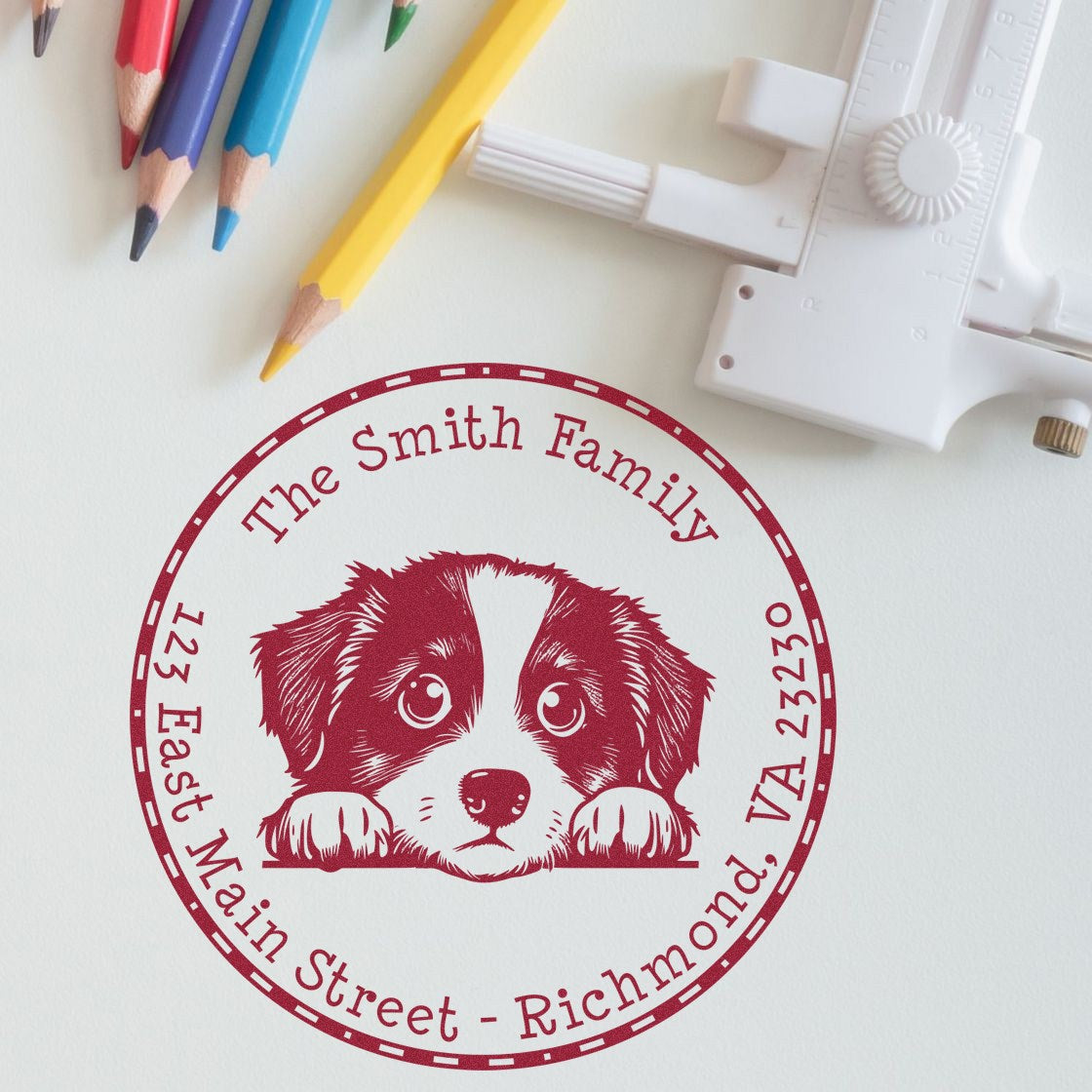 Circular red custom family seal stamp with puppy design, white embossing tool, and colored pencils on a light background.