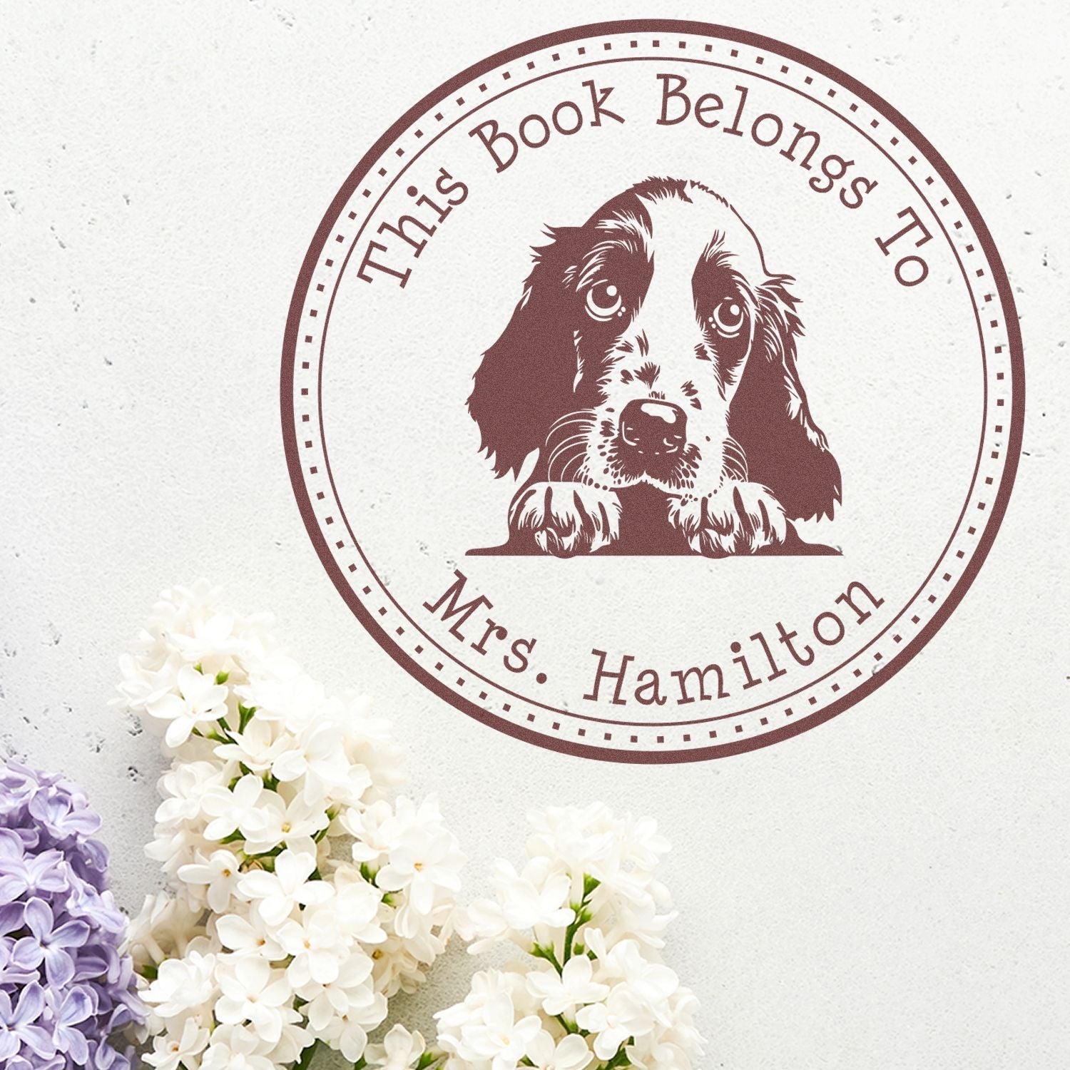 Brown circular book plate stamp and seal with a dog illustration, on white paper with white and lavender flowers.
