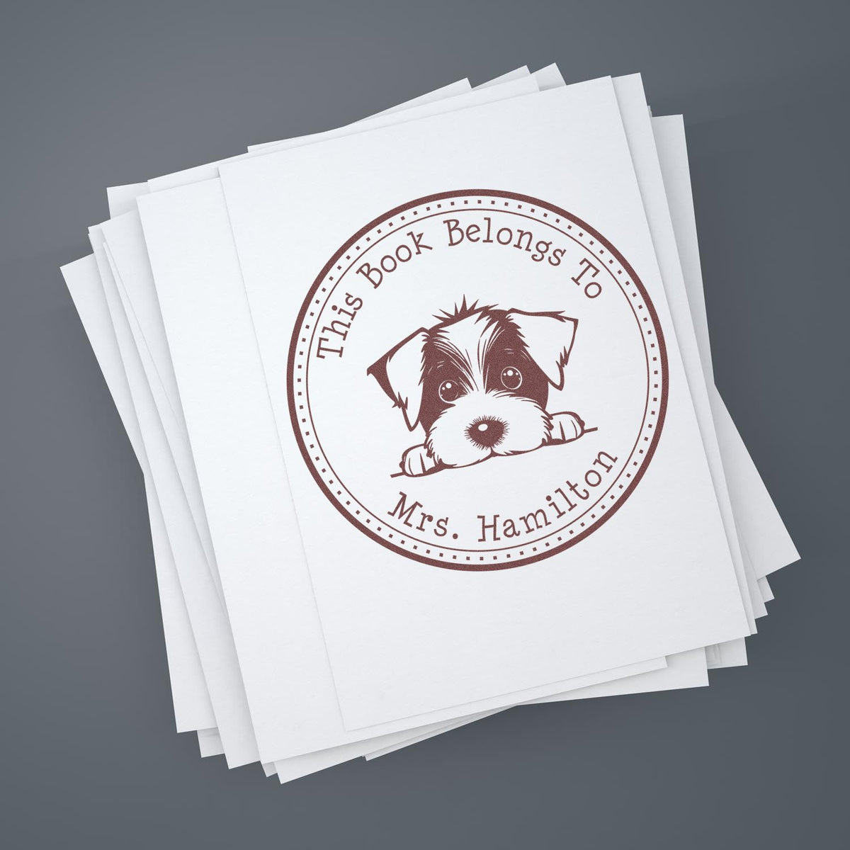 Stack of white sheets with brown circular stamp seal featuring a puppy and This Book Belongs to Mrs. Hamilton text.