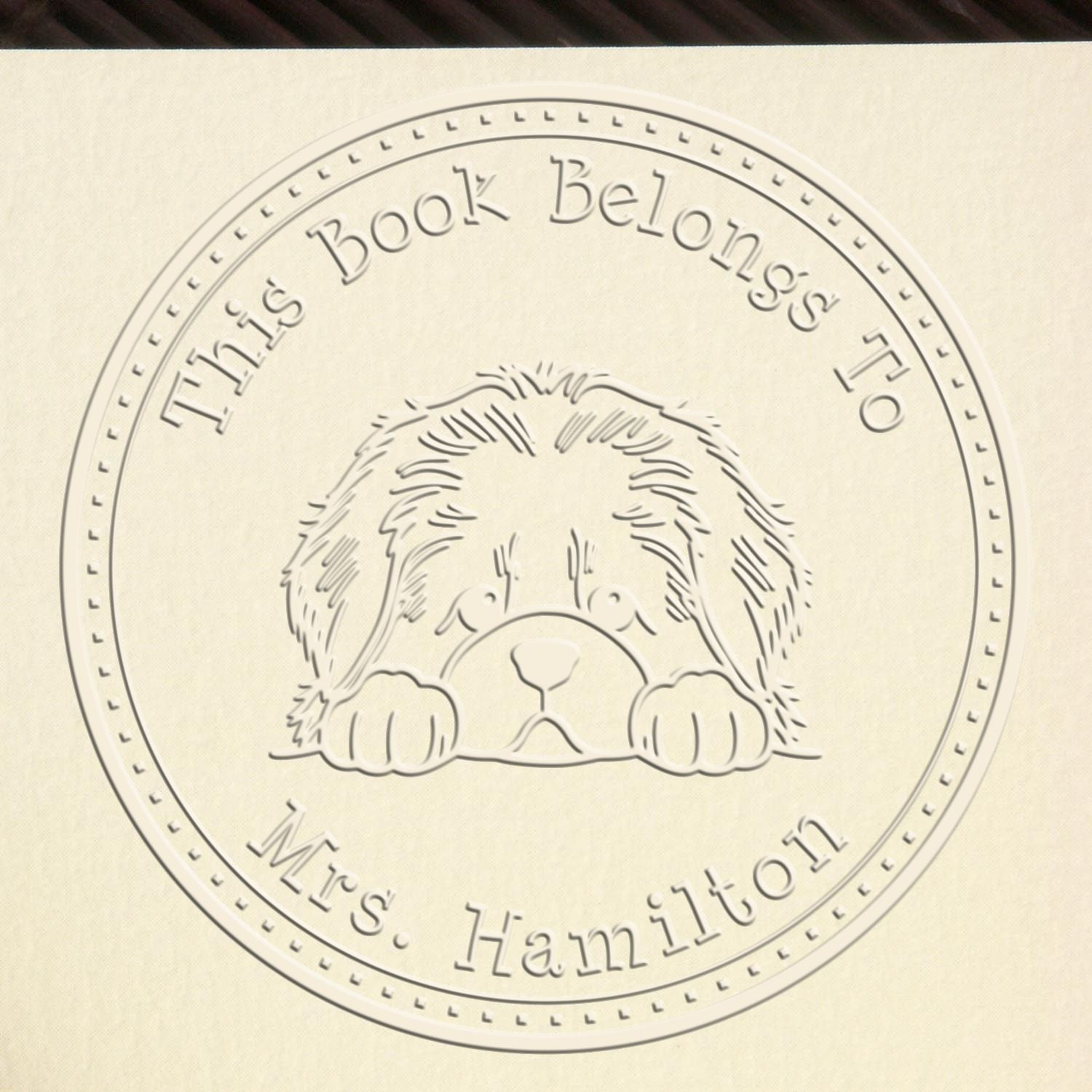 Cream embossed personalized book stamp seal with dog, circular text: This Book Belongs to Mrs. Hamilton.