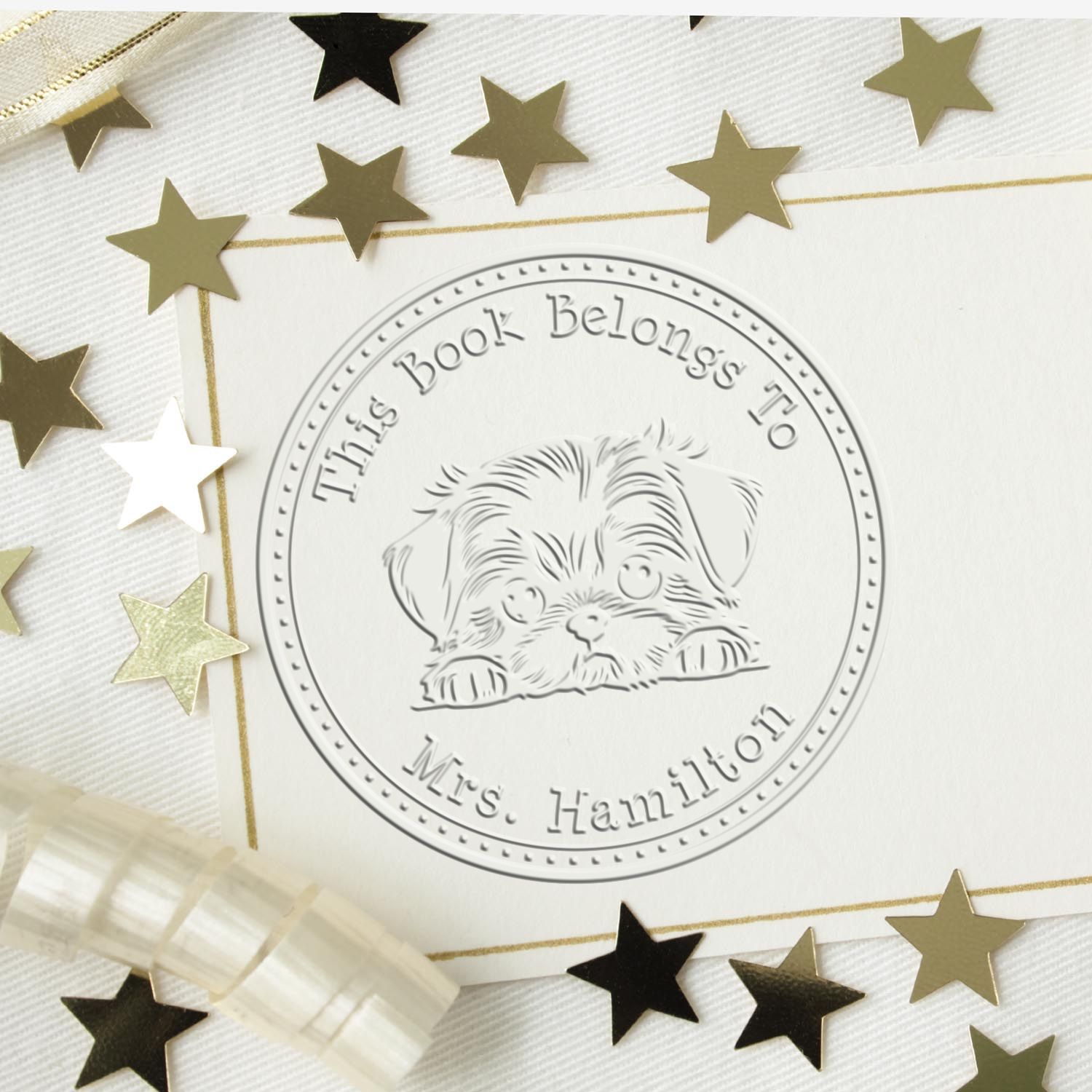 Embossed bookplate stamp with puppy seal reading This Book Belongs To Mrs. Hamilton, on white card with gold stars.