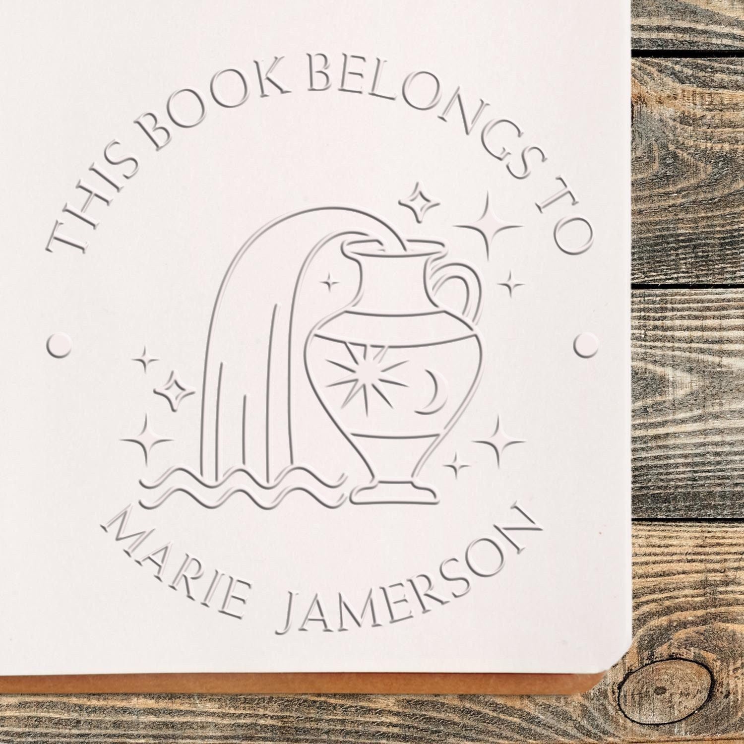 White embossing stamp seal with jug and sparkles, reading This Book Belongs to Marie Jamerson.