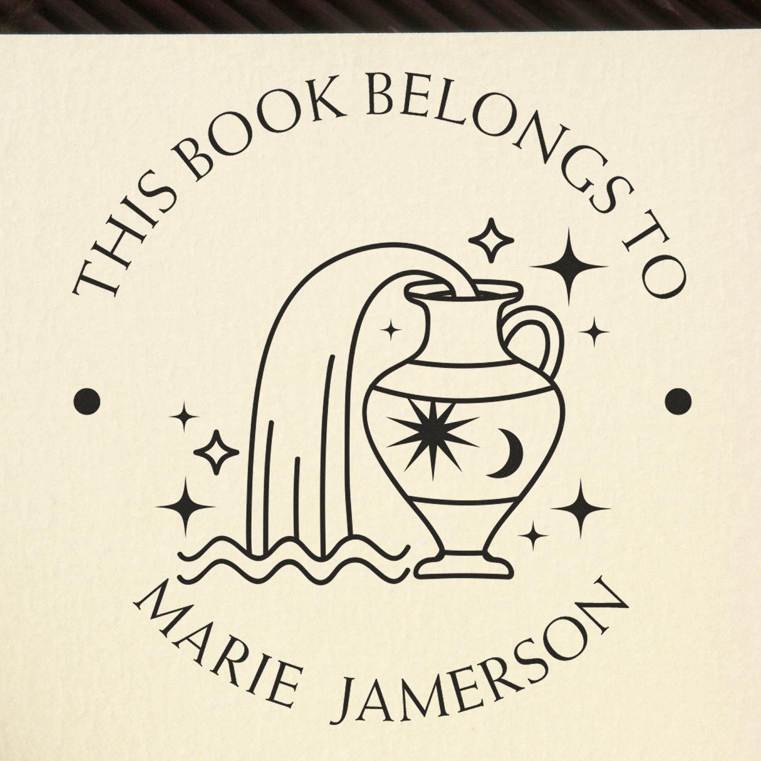 Black custom stamp seal reading This Book Belongs to Marie Jamerson with moon vase, stars, and cream background.