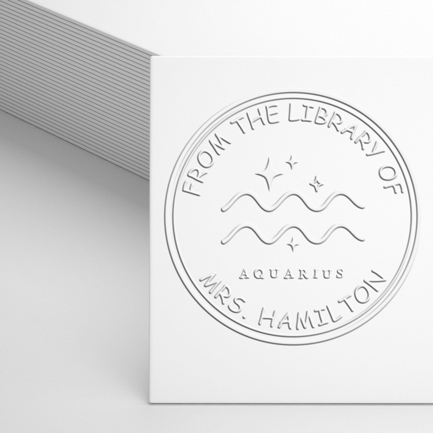 White embossed library ownership seal stamp with Aquarius symbol and circular text for Mrs. Hamilton, on a light gray background.