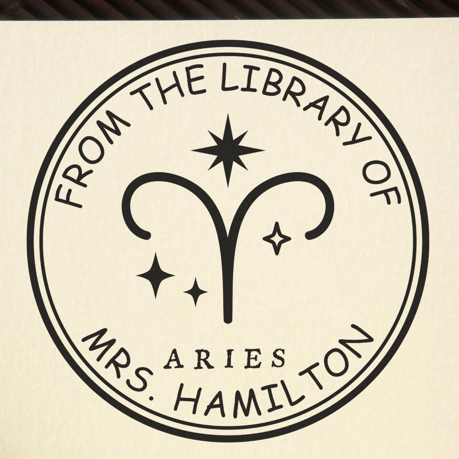 Black Aries library seal stamp reading From the Library of Mrs. Hamilton with stars on a beige background