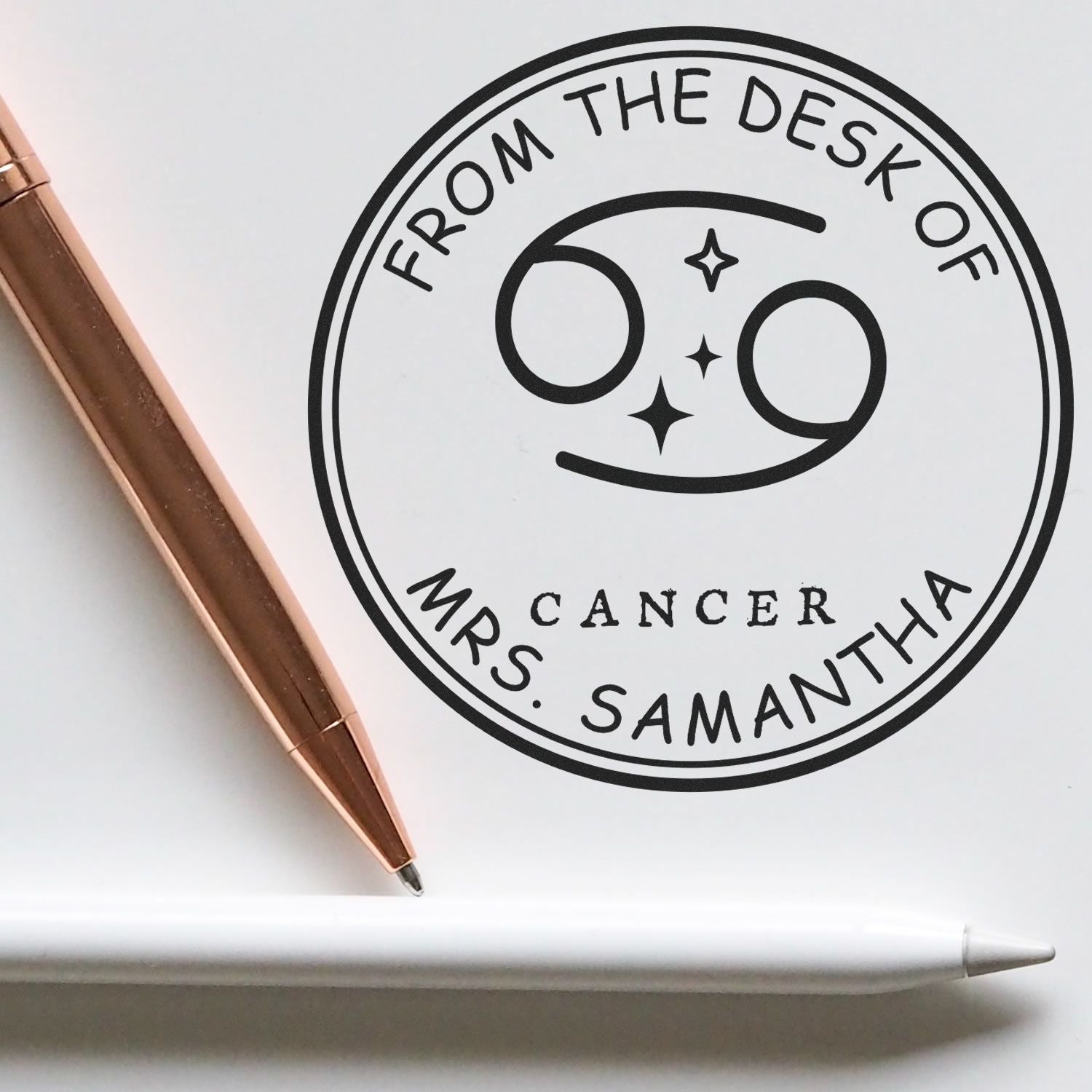 Custom black circular stamp seal for Mrs. Samantha Cancer, with From the Desk of text, star accents, beside a rose-gold pen.