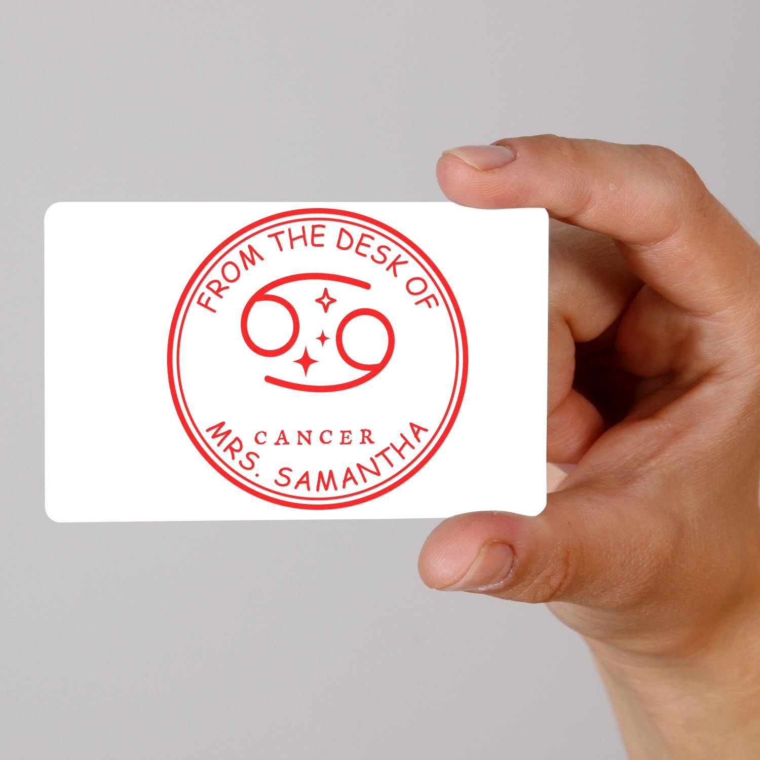 Hand holding white card with red custom stamp seal reading From the Desk of Mrs. Samantha and Cancer zodiac symbol.