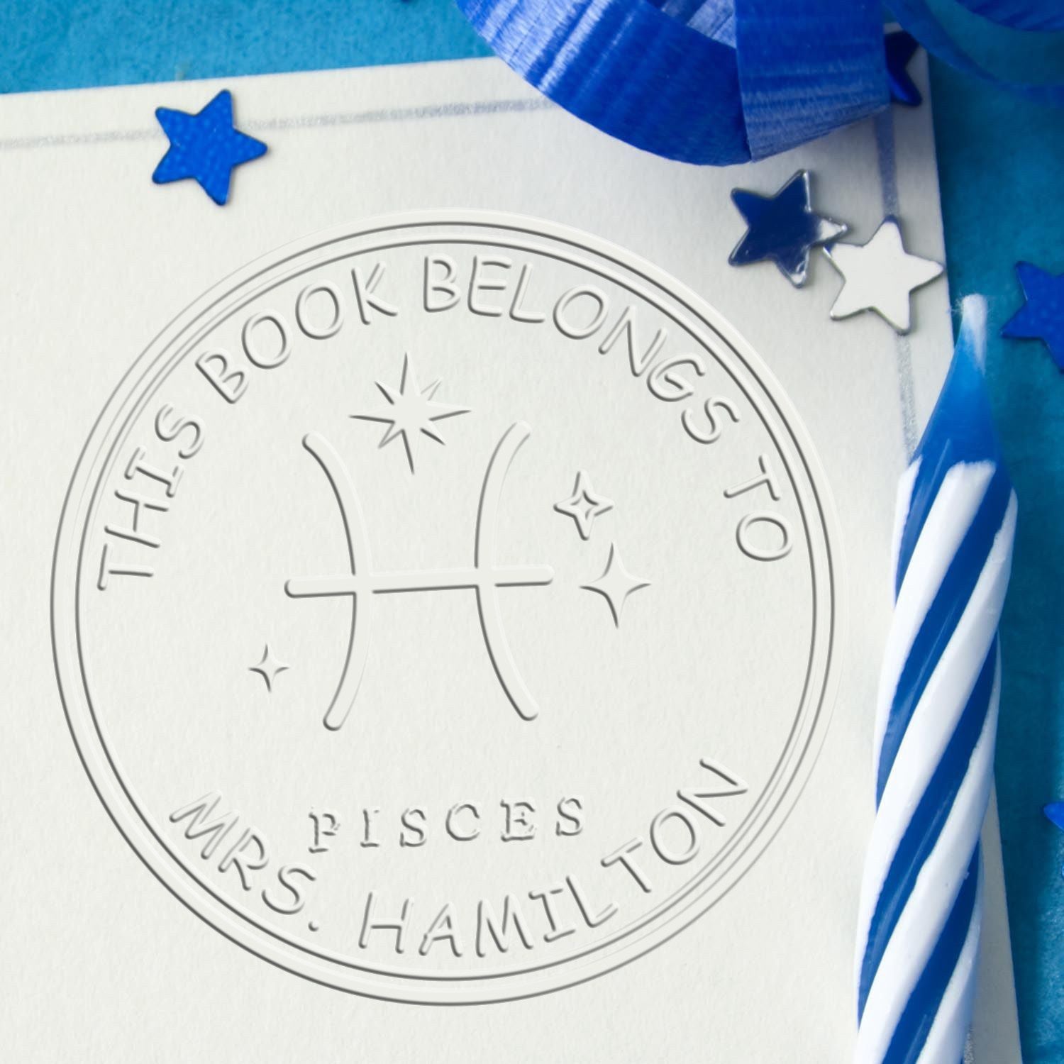 Embossed white custom book seal stamp with Pisces symbol, blue stars, and ribbon accents.