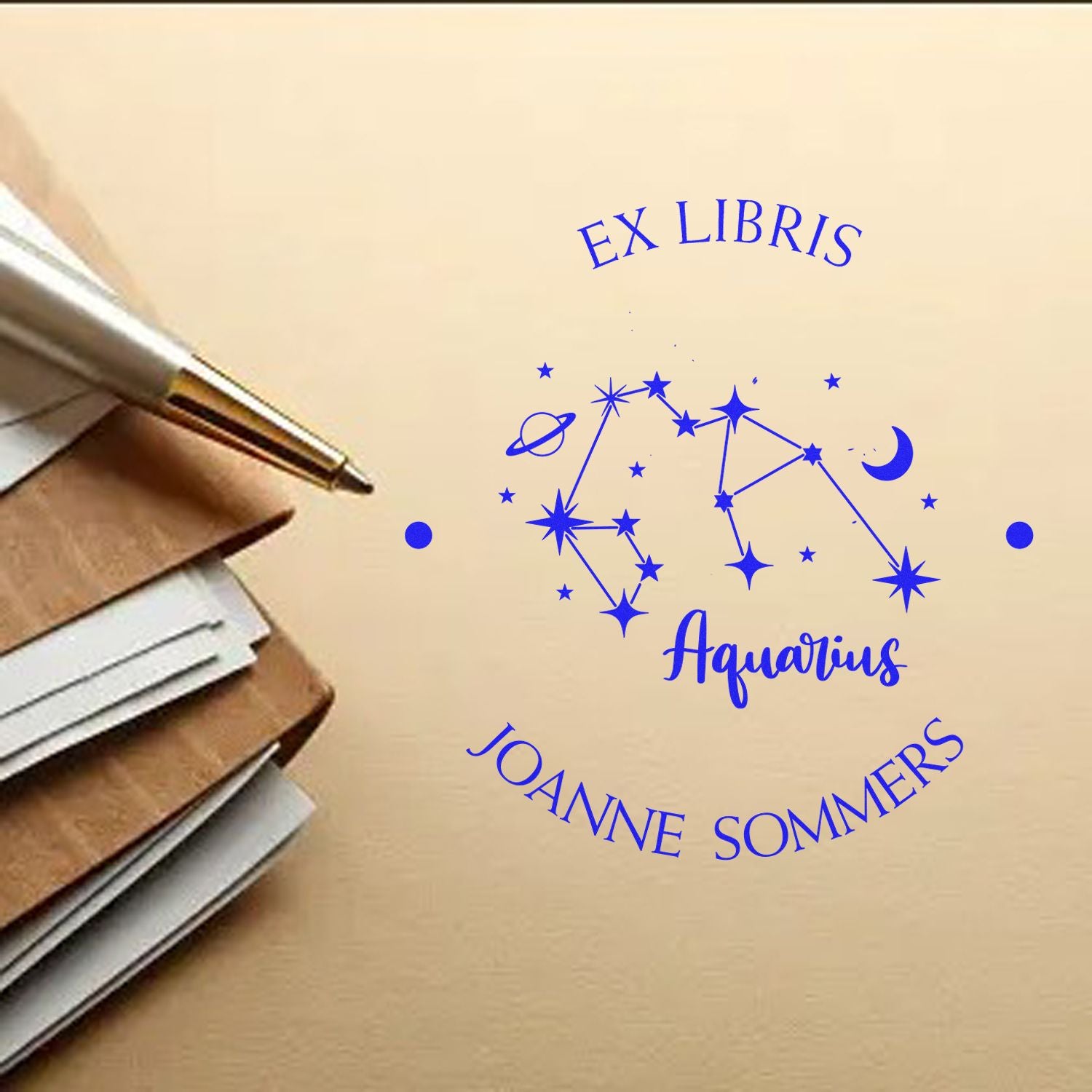Blue Aquarius Ex Libris stamp seal with constellation stars and crescent moon beside a pen on beige paper.