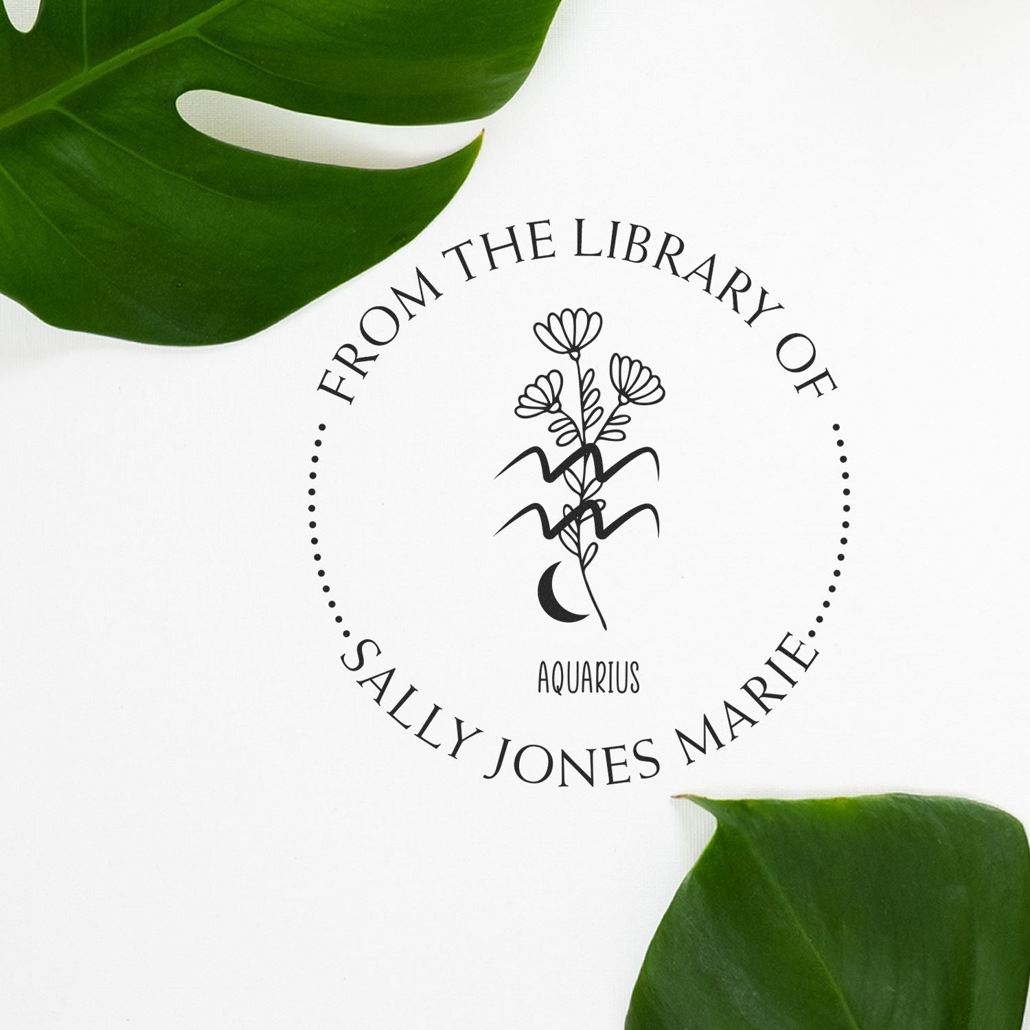 Black custom library stamp seal with Aquarius floral design and Sally Jones Marie text, framed by green leaves on white.
