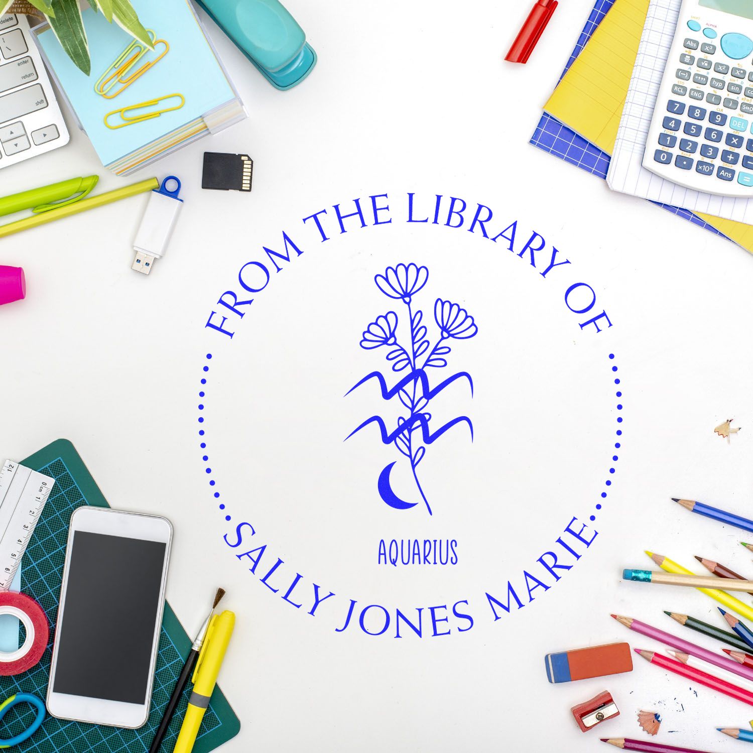 Blue custom library stamp seal reading Sally Jones Marie, with Aquarius symbol, on a white desk with colorful stationery.