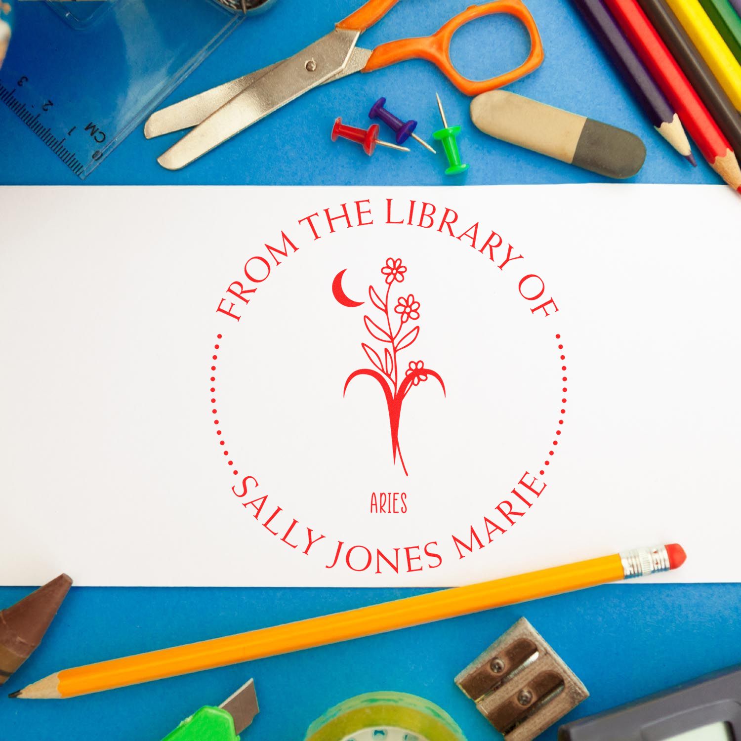 Red custom library seal with Aries floral emblem on white card, surrounded by school supplies on blue background
