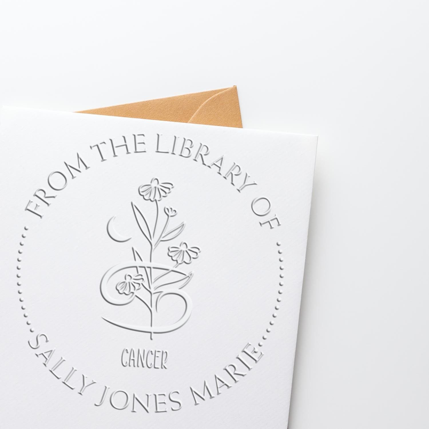 White embossed library stamp seal with floral Cancer monogram and tan envelope, personalized for Sally Jones Marie.