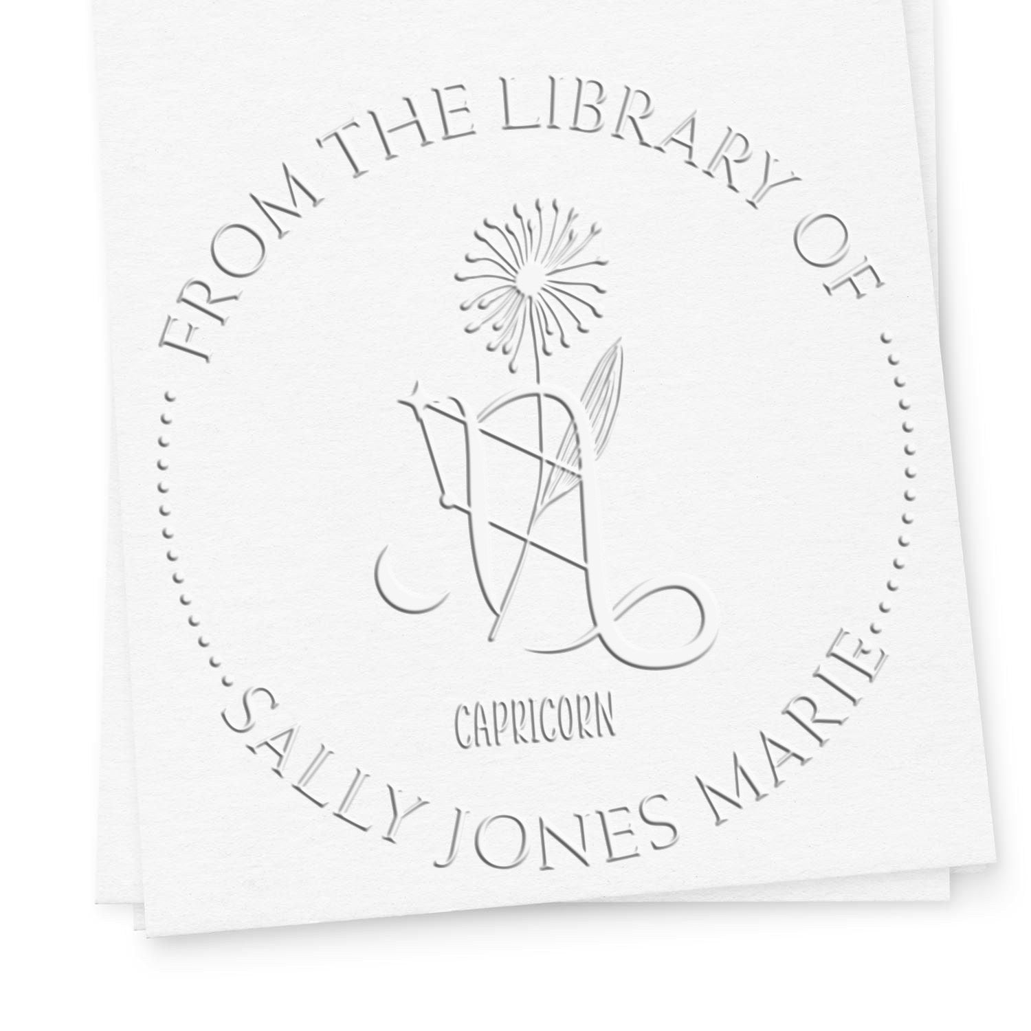 White embossed library stamp seal with circular text, floral emblem, and Capricorn name design.