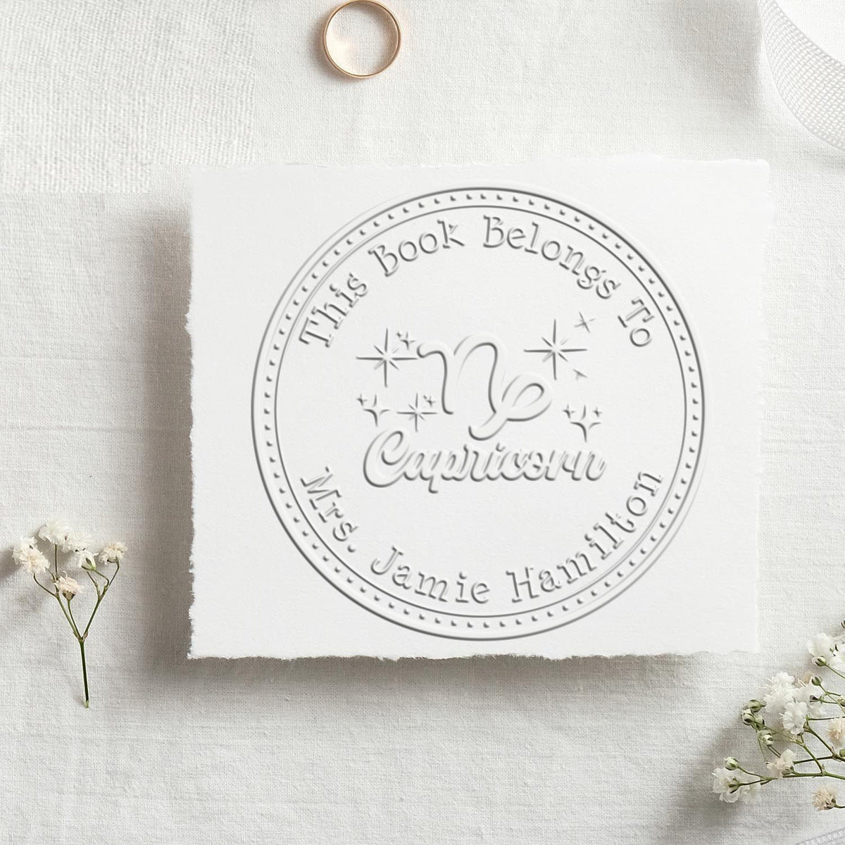 Shiny Capricorn zodiac symbol personalized book embosser with scripted font, showing the embossed seal in use.