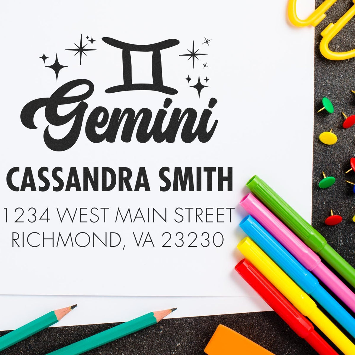 Black Gemini self-inking stamp and seal with Cassandra Smith address, framed by colorful pens and pencils.