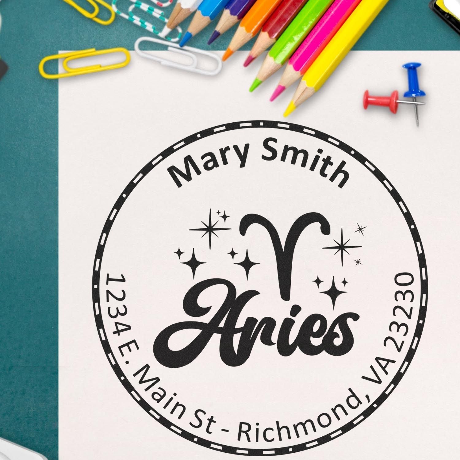 Custom black circular seal stamp for Mary Smith, with sparkles, on white paper beside colorful pencils and paper clips.