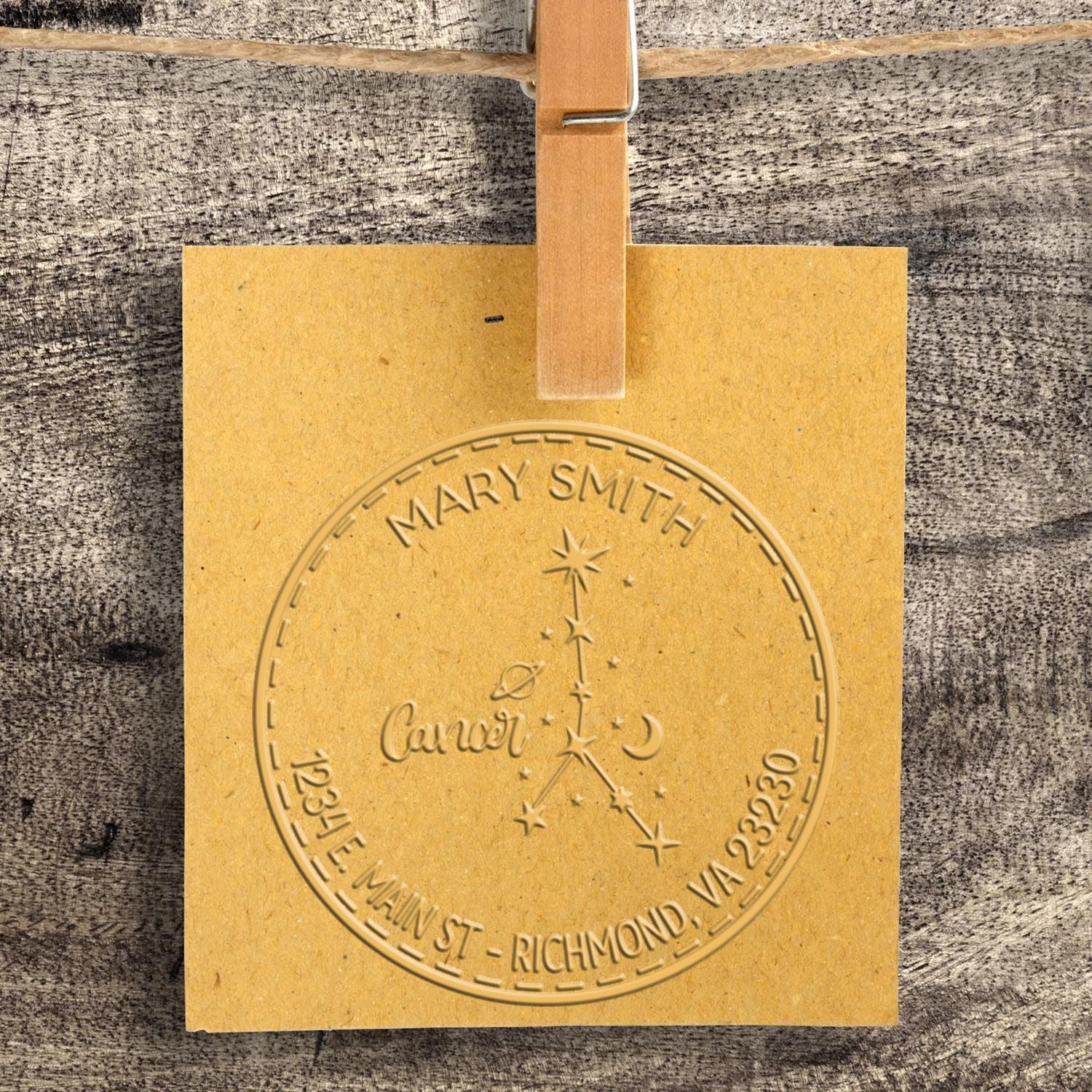 Yellow embossed seal stamp hanging from a wooden clip, with Mary Smith Cancer constellation design and Richmond, VA text.