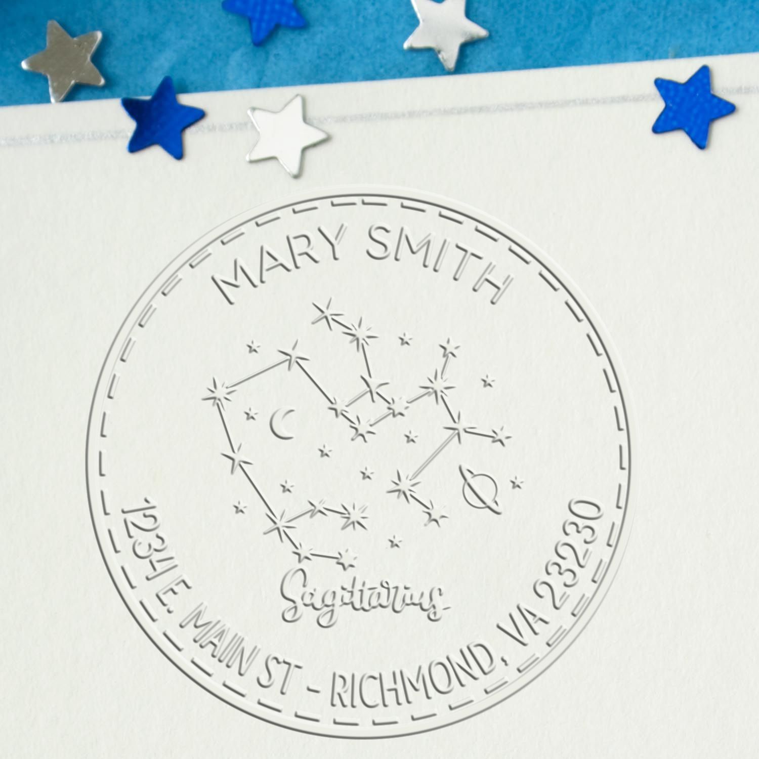 Embossed silver seal stamp with Mary Smith and Sagittarius constellation, on white paper with blue and silver star confetti.