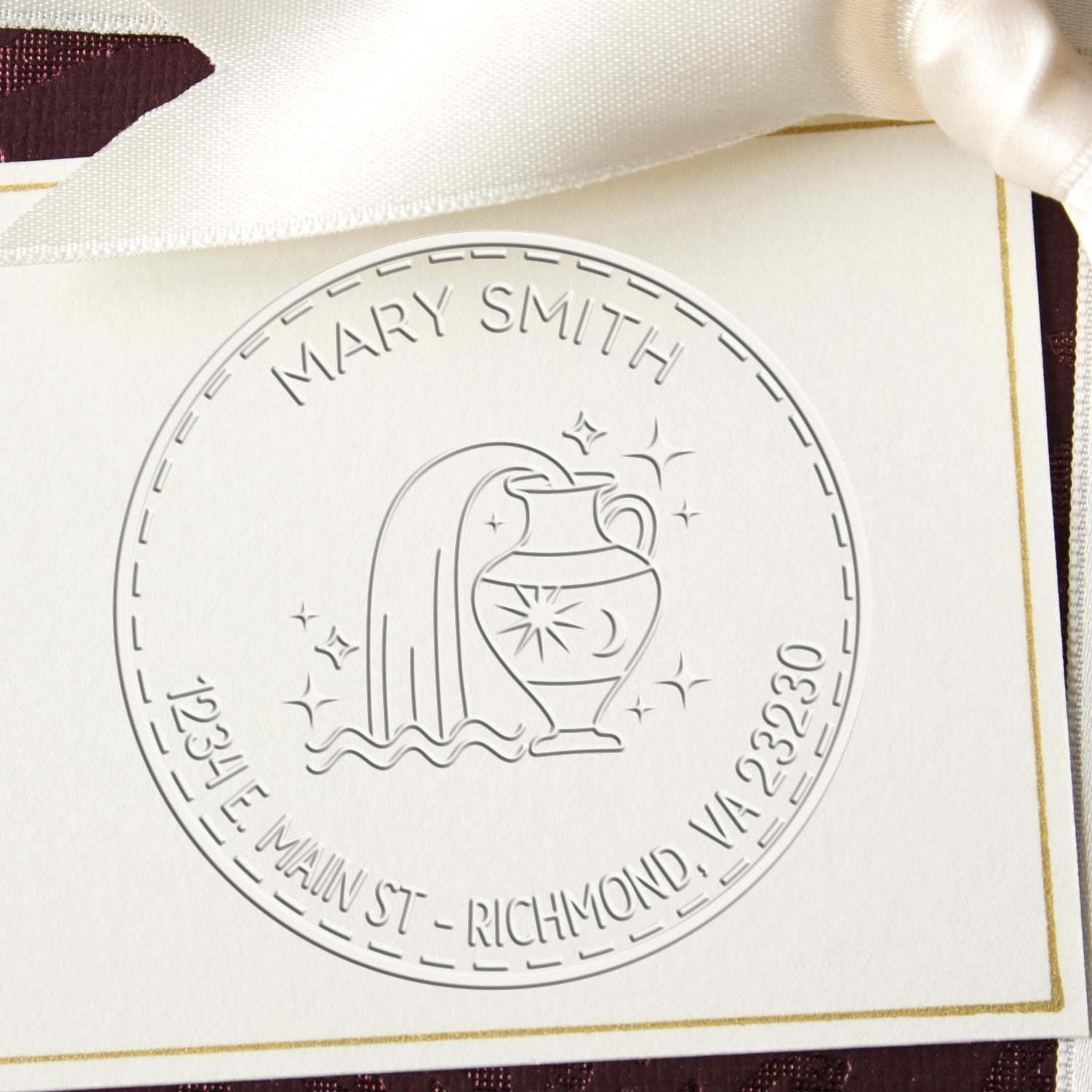 White embossed Mary Smith memorial stamp seal with urn, waterfall and stars on a cream card with satin ribbon.