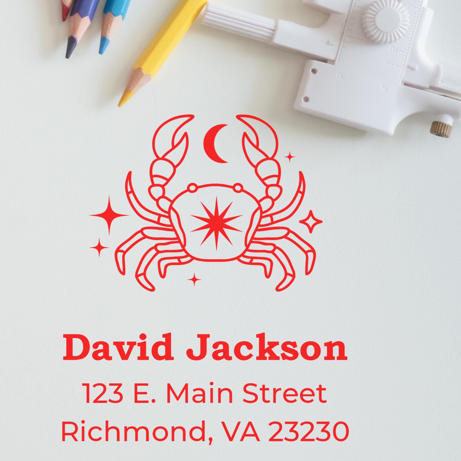 Red crab seal stamp with crescent moon and stars, beside colored pencils and a white embosser; David Jackson address below.