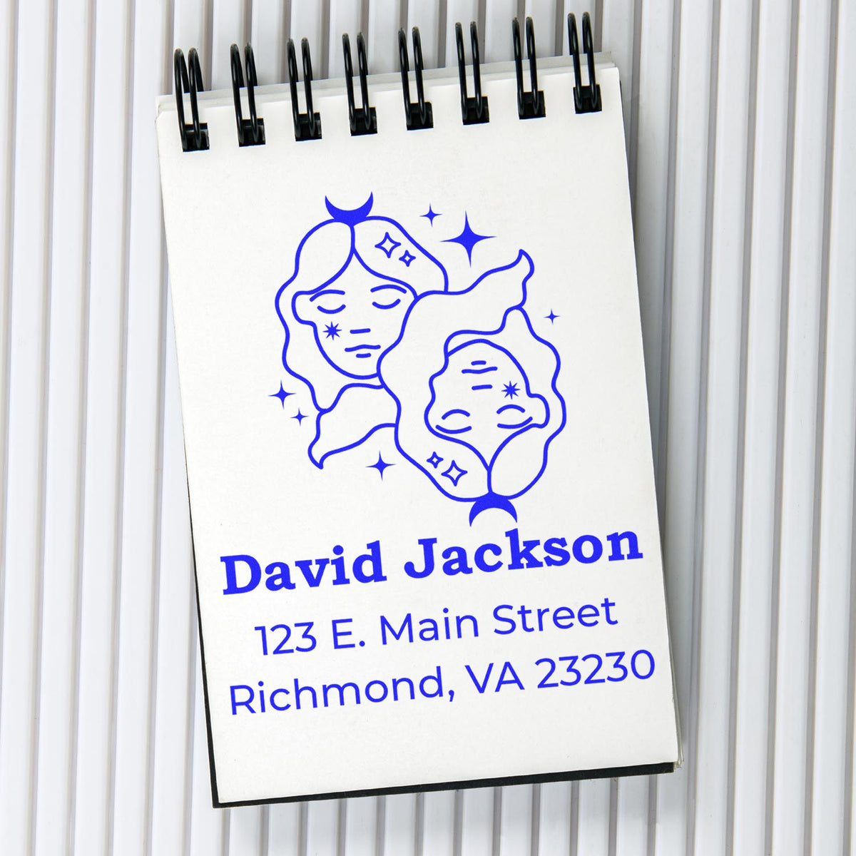 Blue custom address stamp and seal design on white spiral notepad, featuring moon faces, sparkles, and Richmond address.