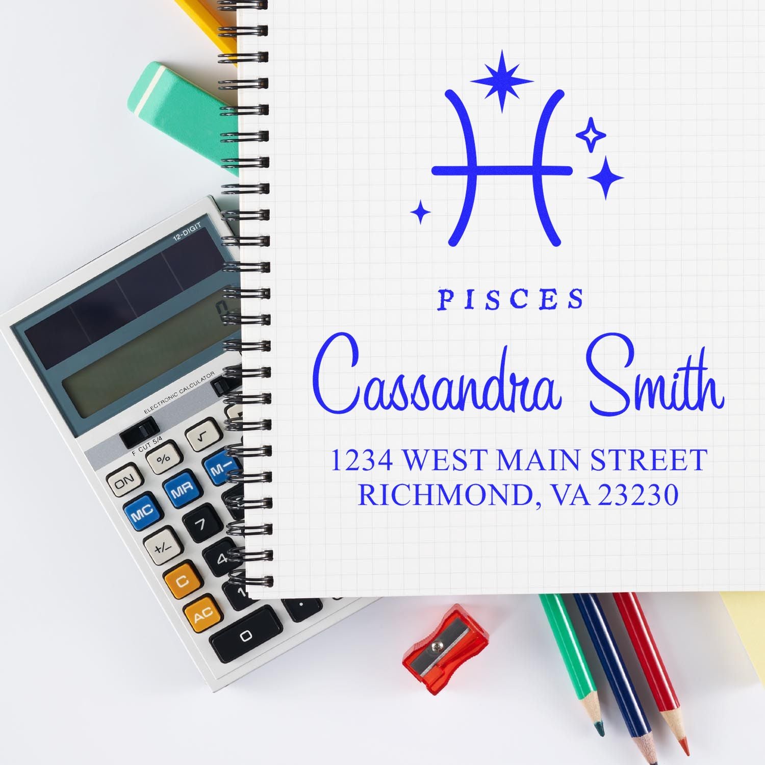 Blue Pisces custom stamp seal with name and Richmond, VA address on graph notebook, beside calculator and pencils.