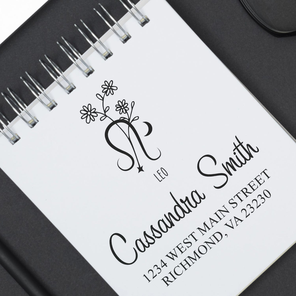 Black custom stamp and seal design on white spiral notebook page, with floral monogram, name Cassondra Smith, and address.